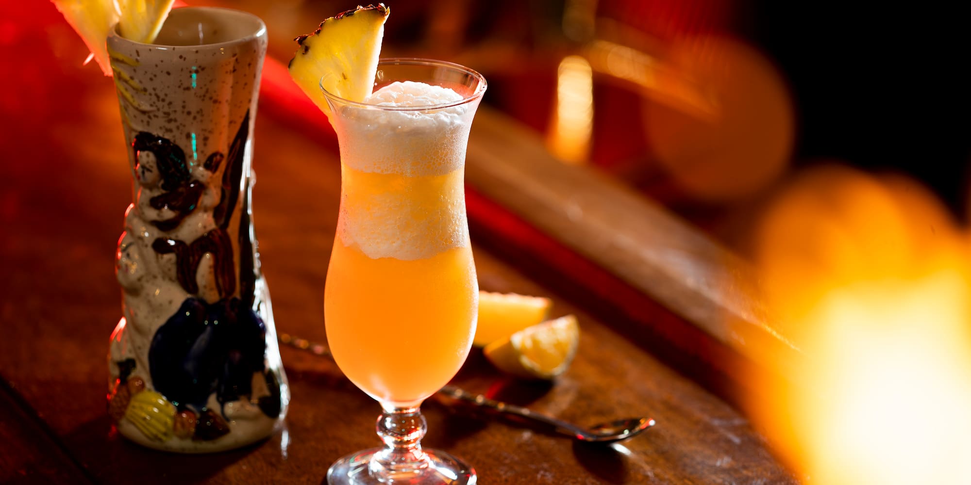 a glass of orange liquid with a slice of pineapple on top of it