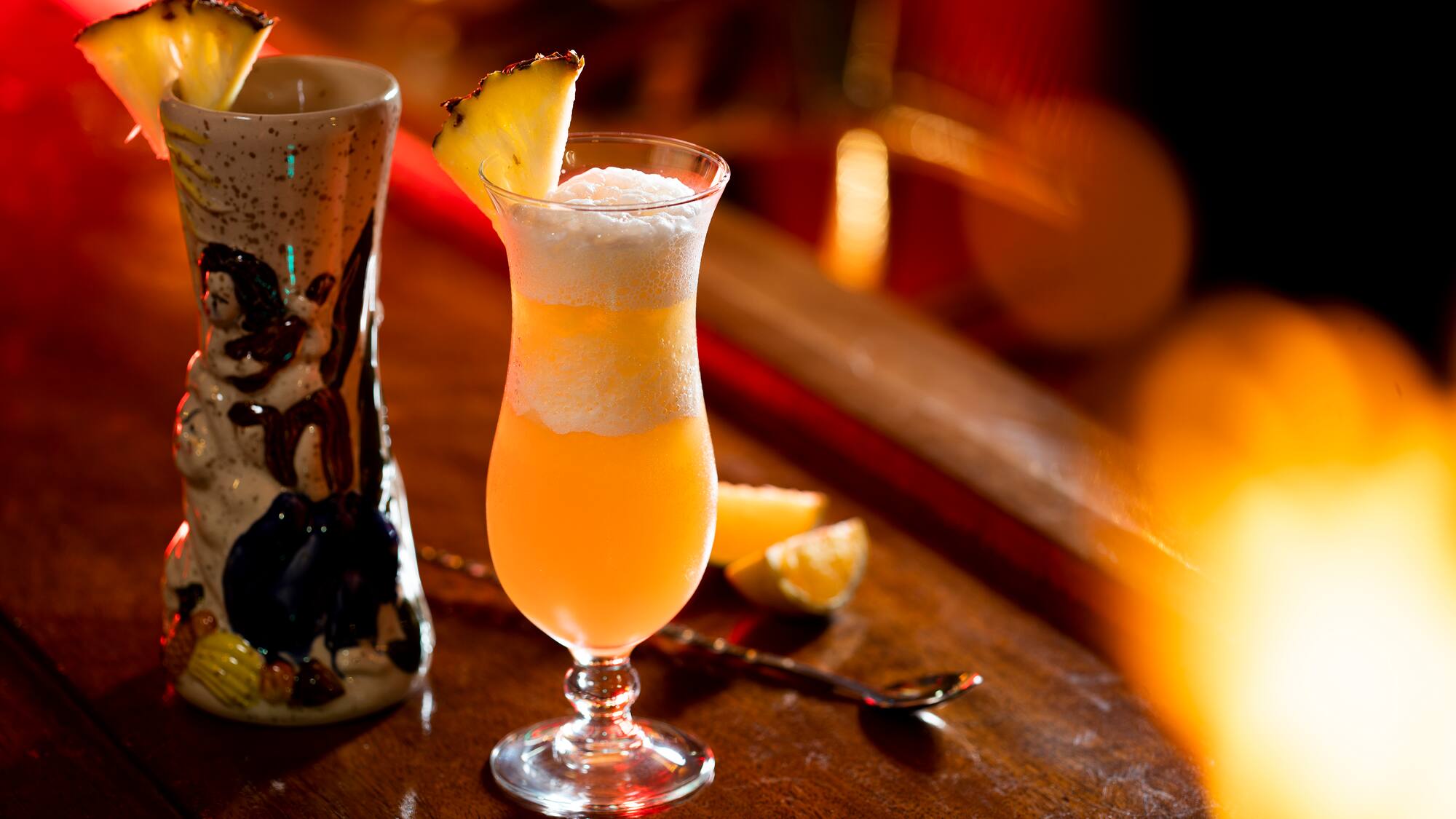 a glass of orange liquid with a slice of pineapple on top of it