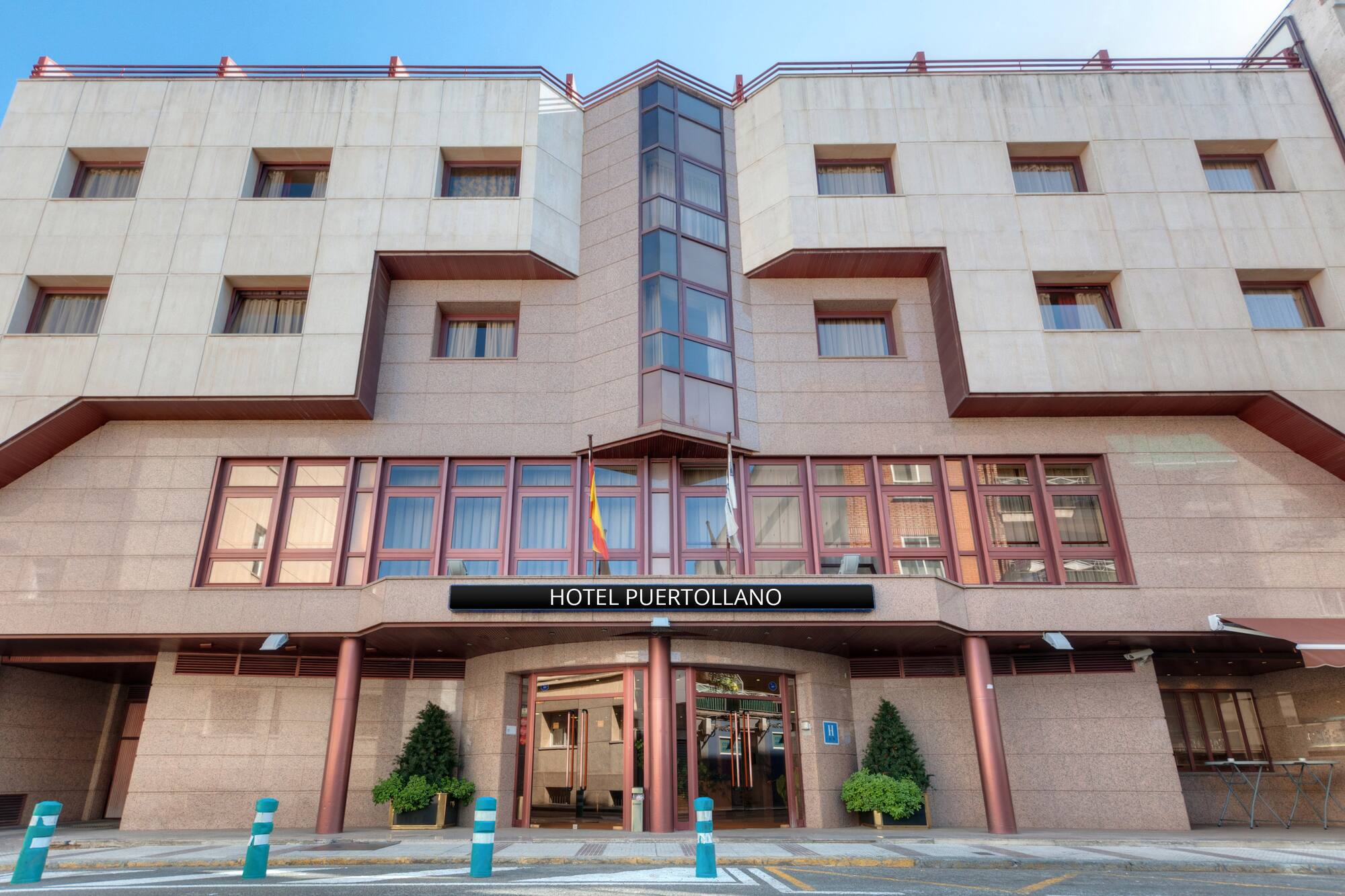 Hotel Puertollano facade with modern design, glass entrance, and flags.