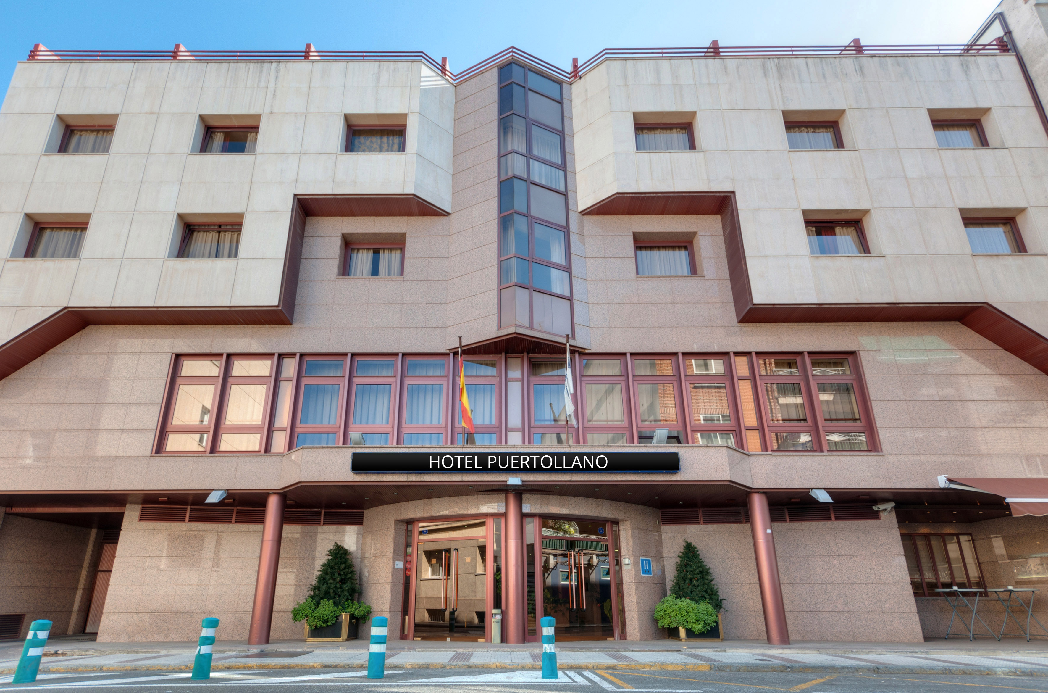 Hotel Puertollano facade with modern design, glass entrance, and flags.