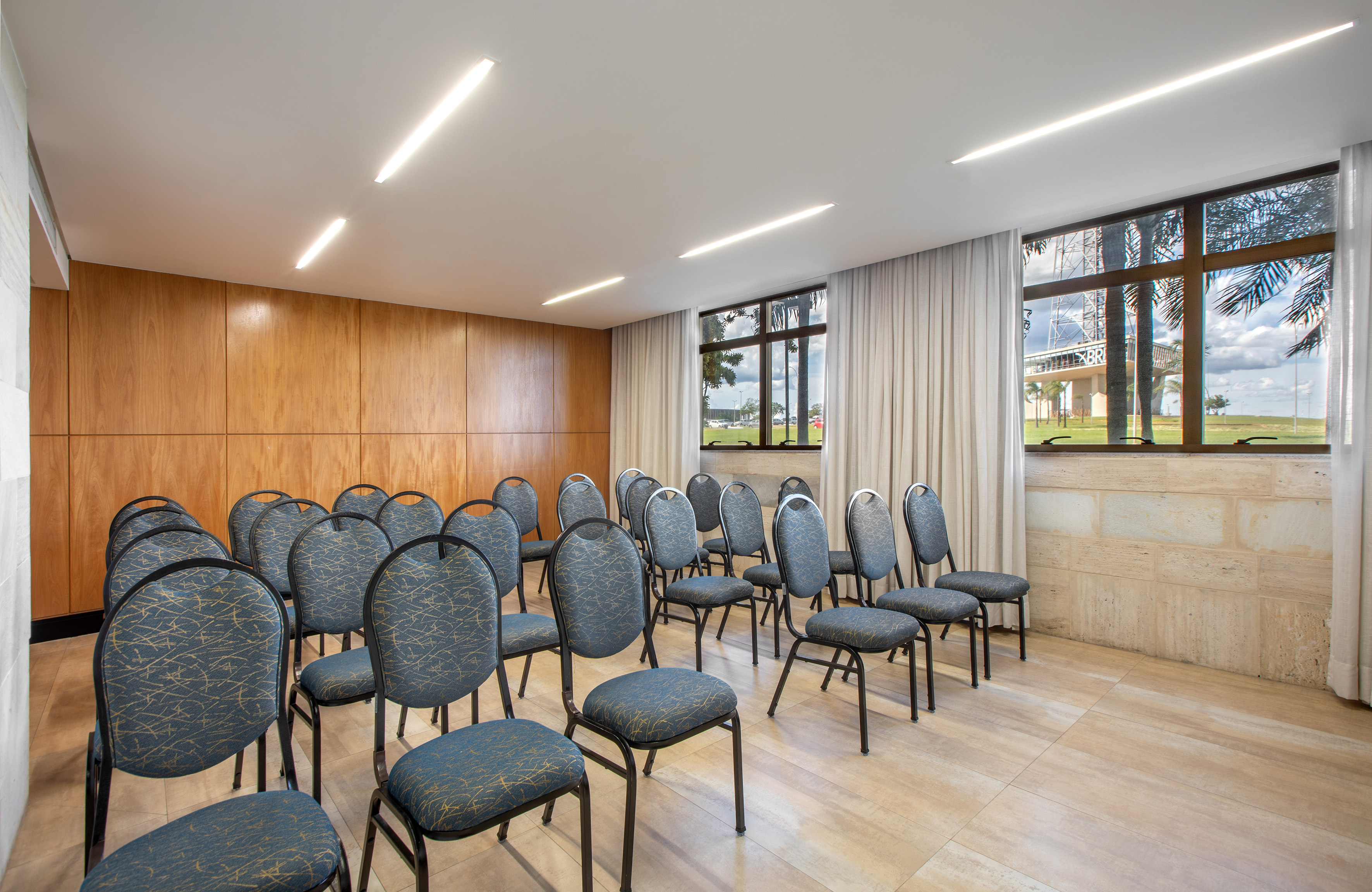 Empty conference room with rows of blue chairs, wood paneling, and large windows.