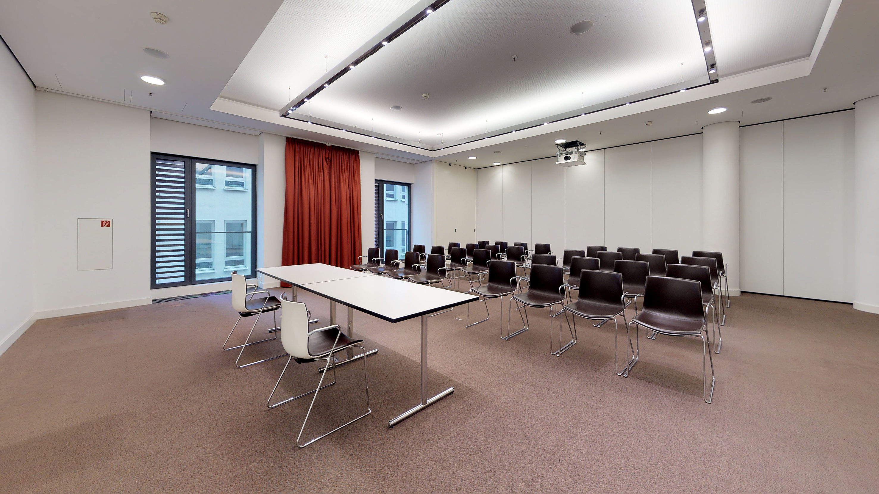 Modern conference room with rows of dark chairs, projector, and long white table.