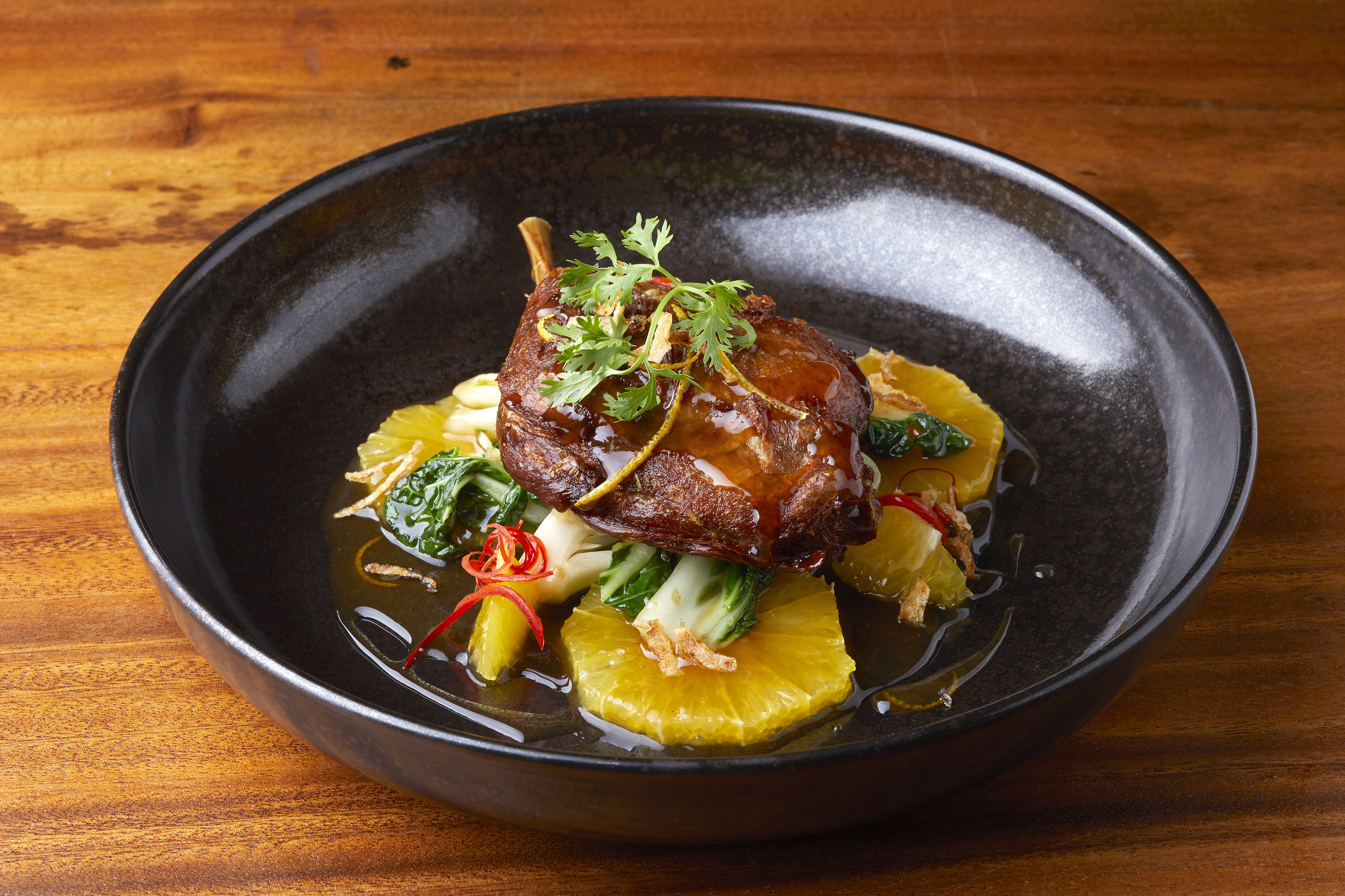 Roasted duck leg, orange slices, bok choy, cilantro, and chili threads.
