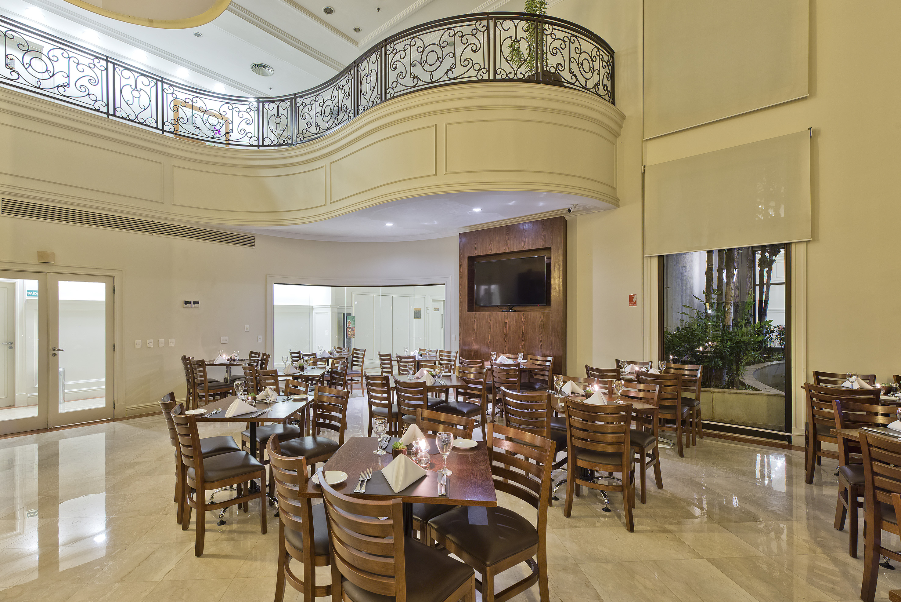 Elegant hotel restaurant dining room with wooden tables, chairs, and ornate balcony.