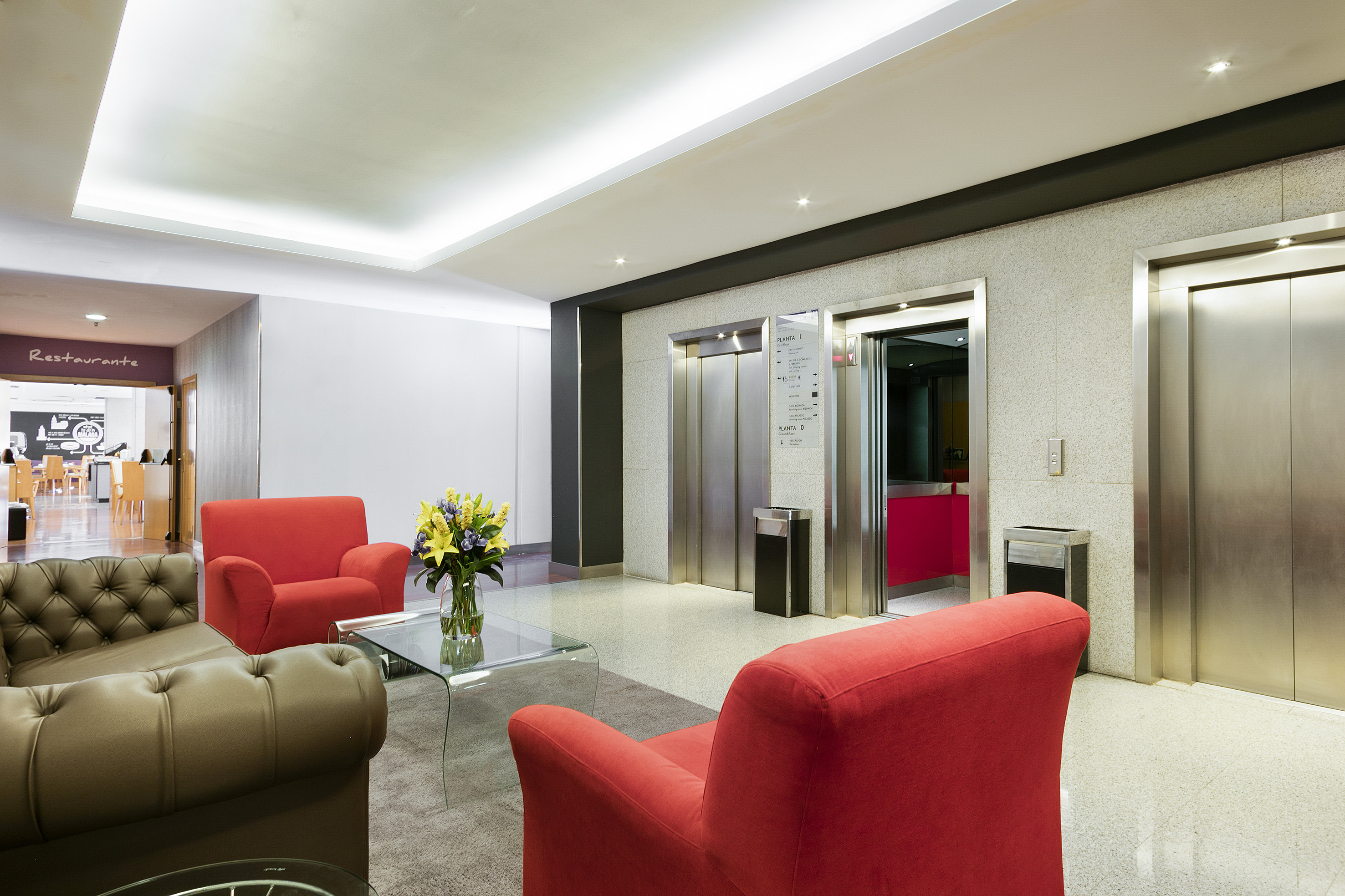 Modern hotel lobby with elevators, red armchairs, and a restaurant.