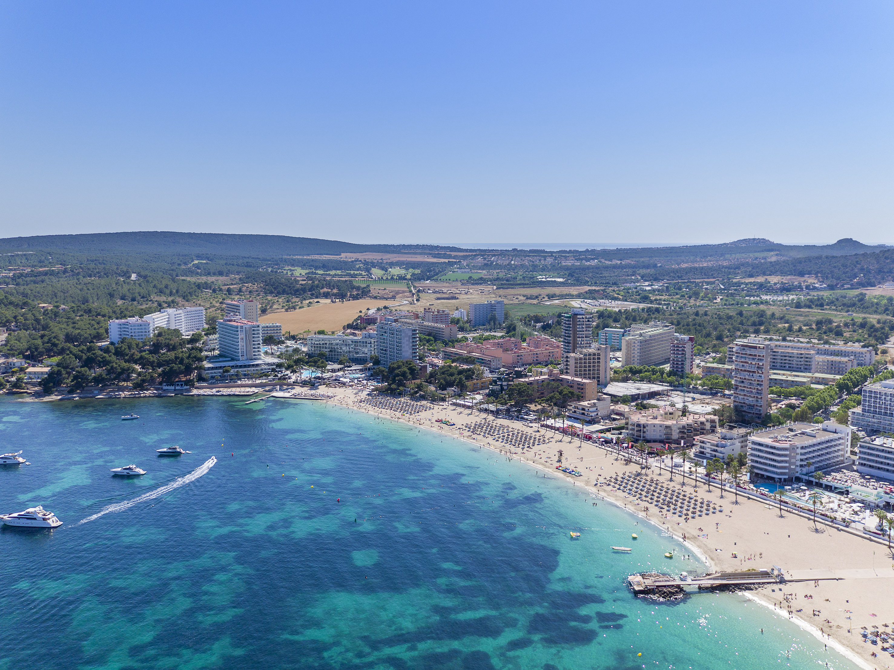 Majorca beach resort aerial view with turquoise sea, boats, and hotels.