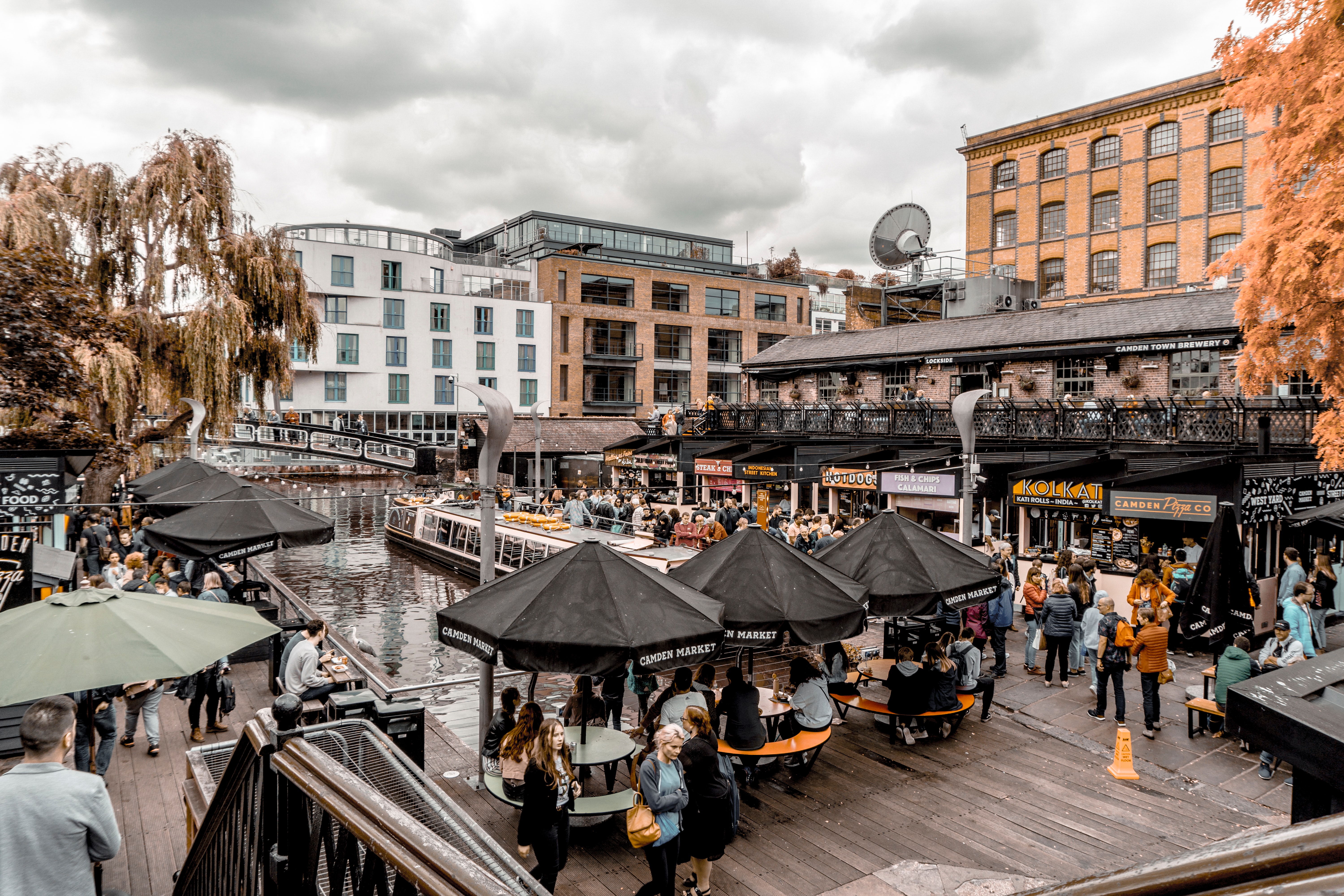 Busy Camden Market canal, people dining at food stalls under umbrellas.