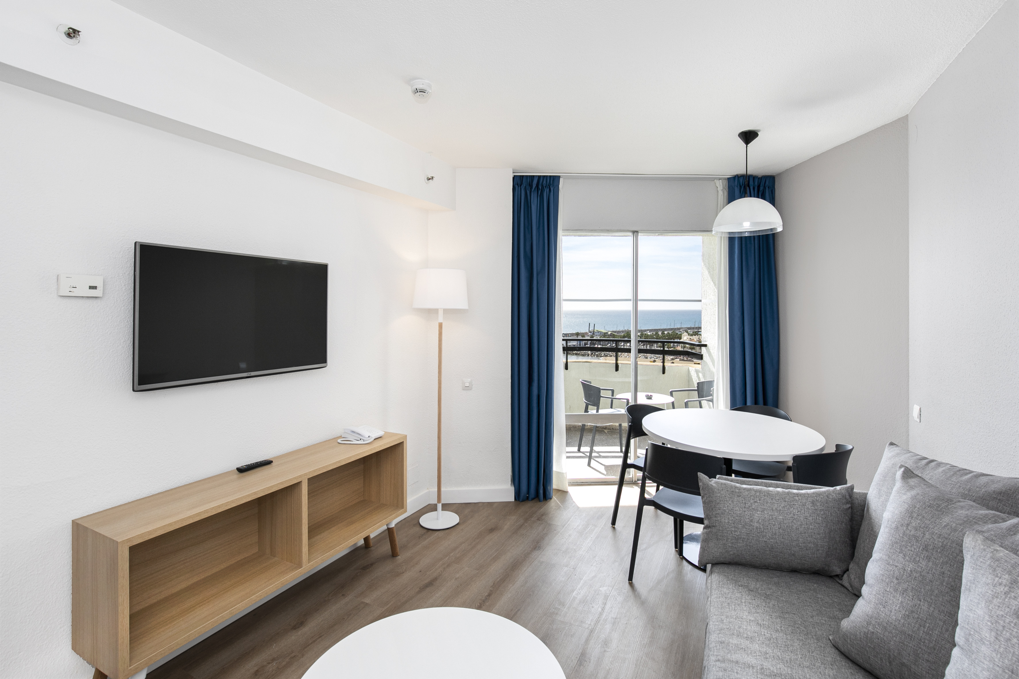 Modern living room with sea view balcony, grey sofa, dining table, and TV.