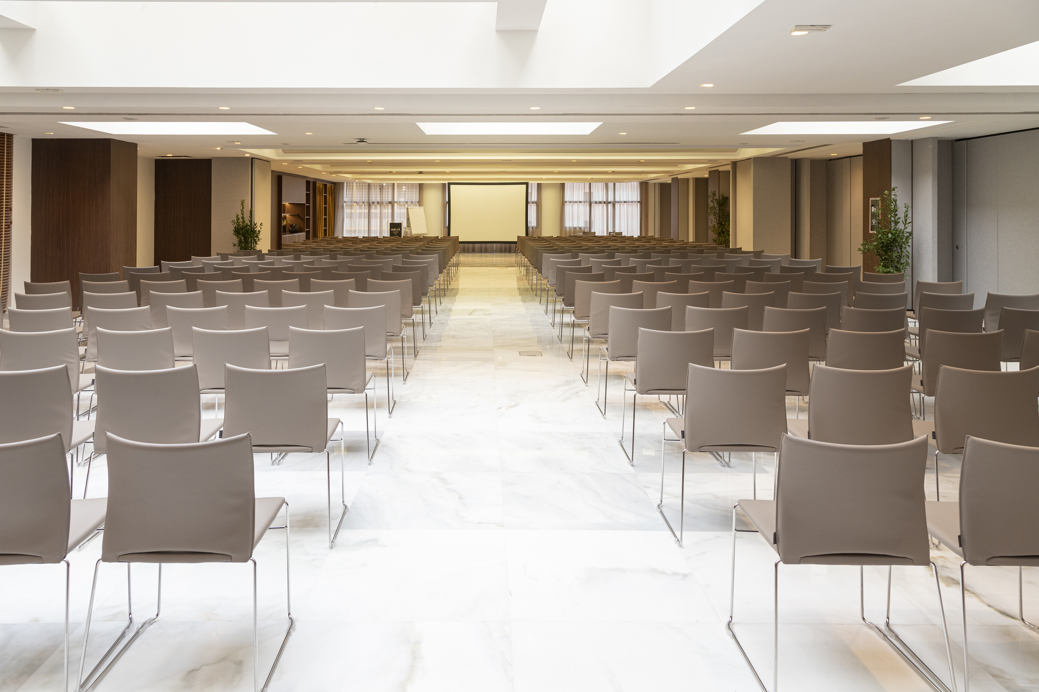 Modern conference room with rows of gray chairs and a projection screen.