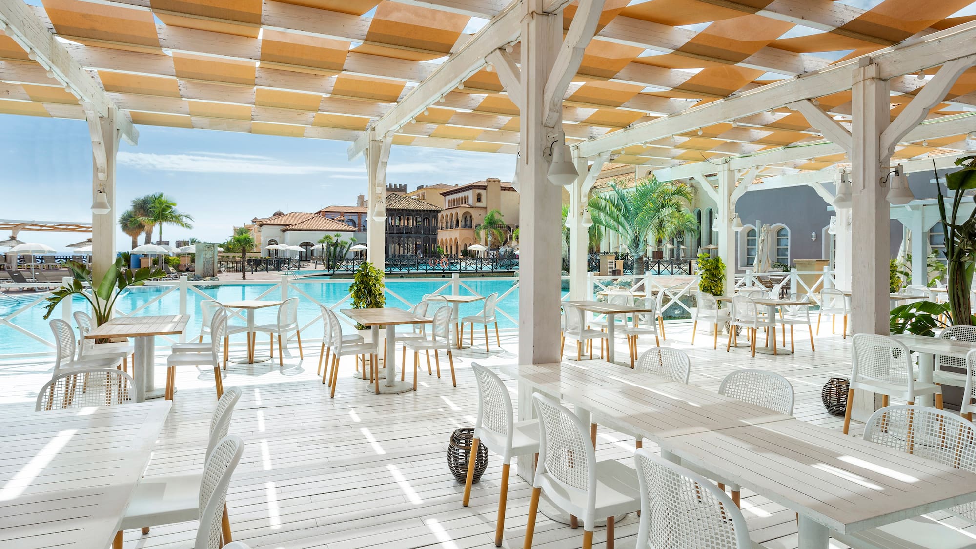 a white patio with tables and chairs and a pool