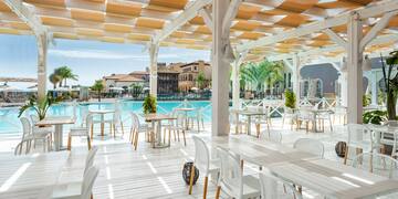 a white patio with tables and chairs and a pool