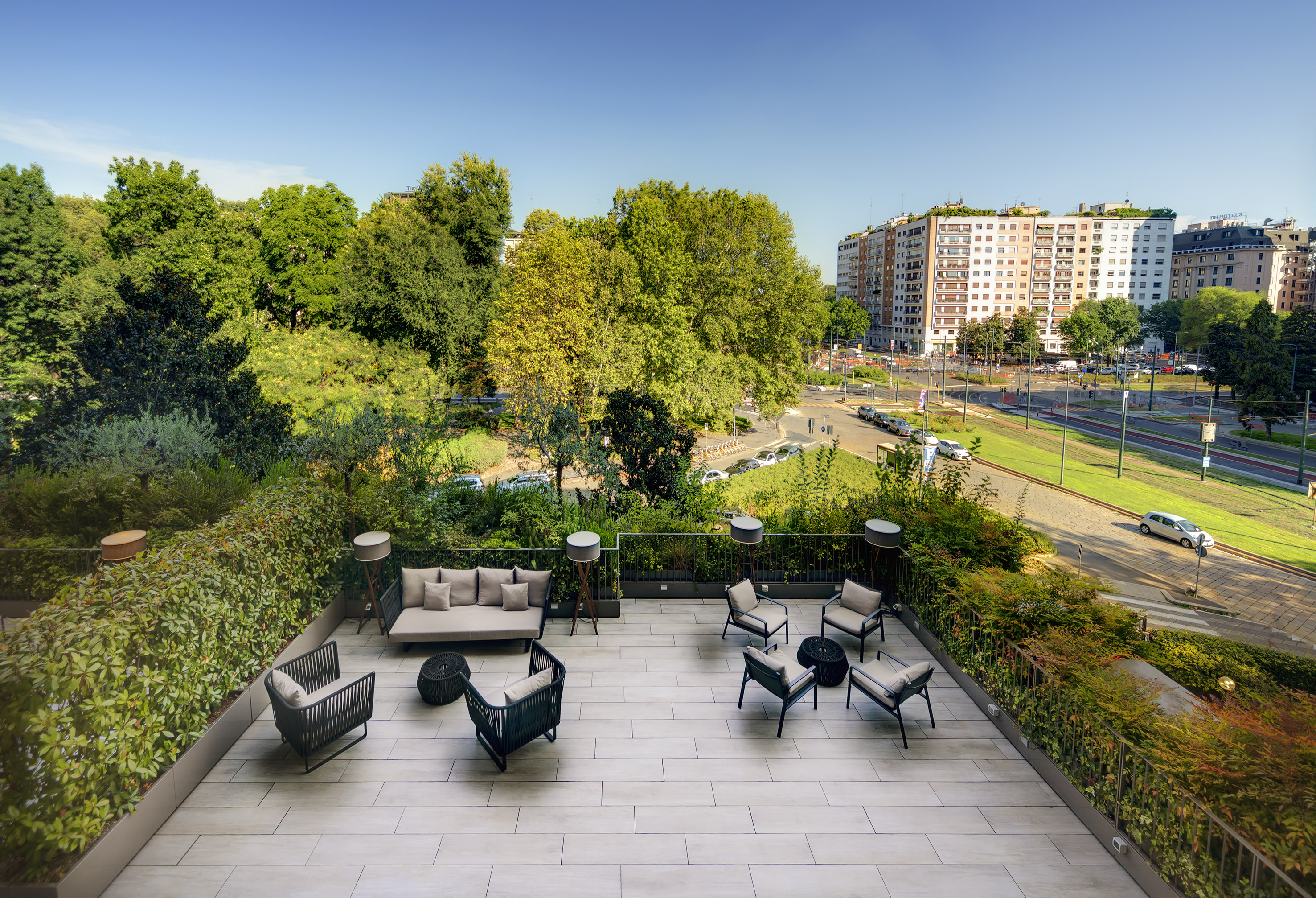 Urban rooftop lounge with modern outdoor furniture, city view, and green trees.