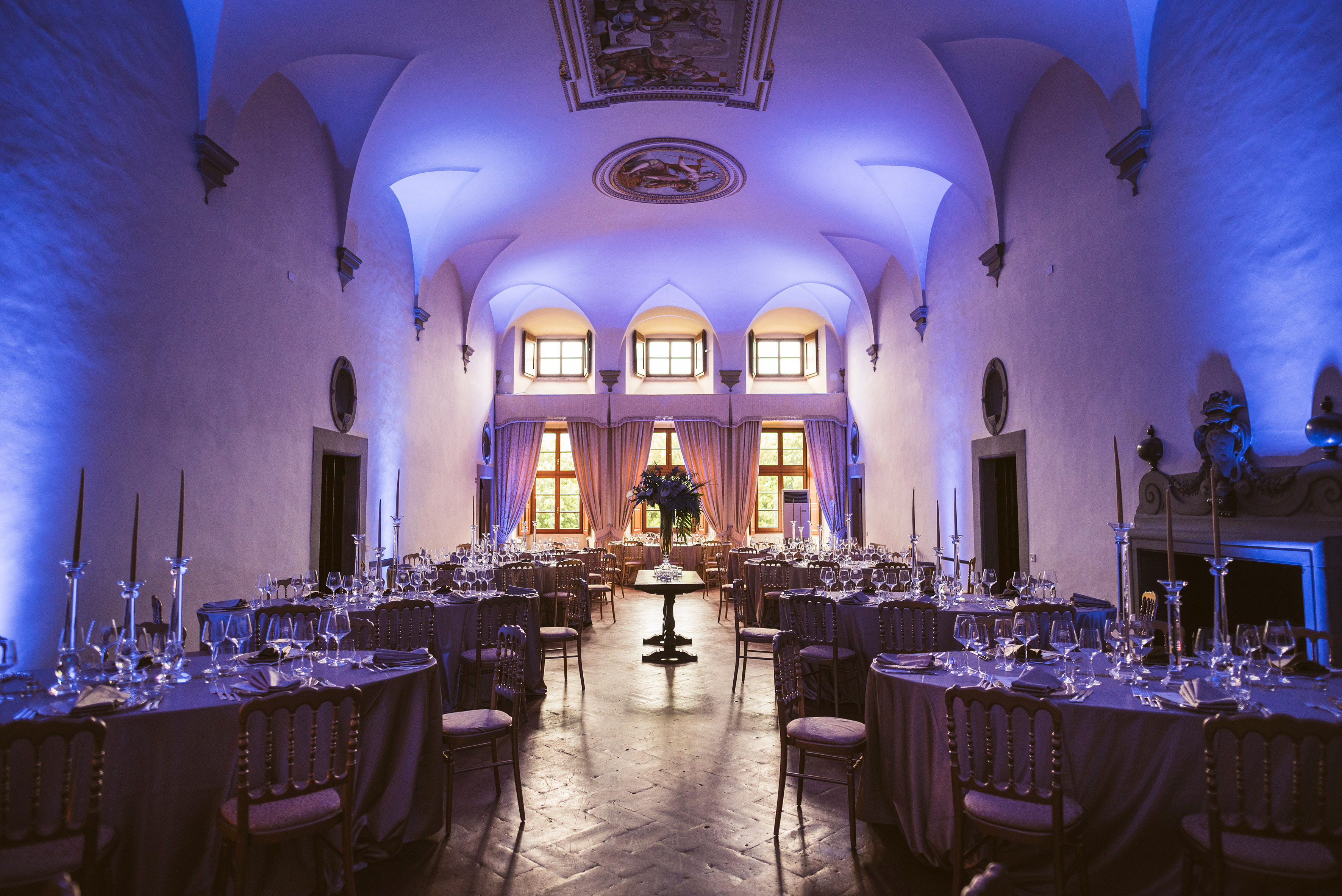 Elegant banquet hall with vaulted ceilings, set tables, blue ambient lighting.