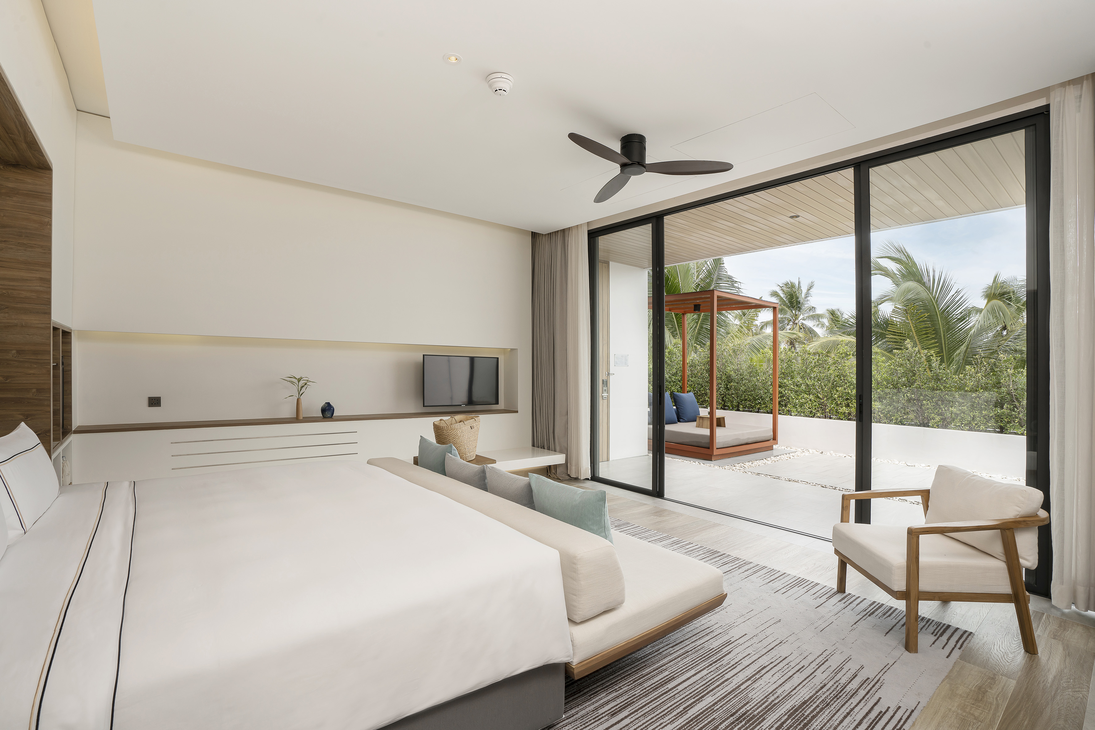 Tropical resort bedroom with modern bed, private patio, and outdoor daybed.