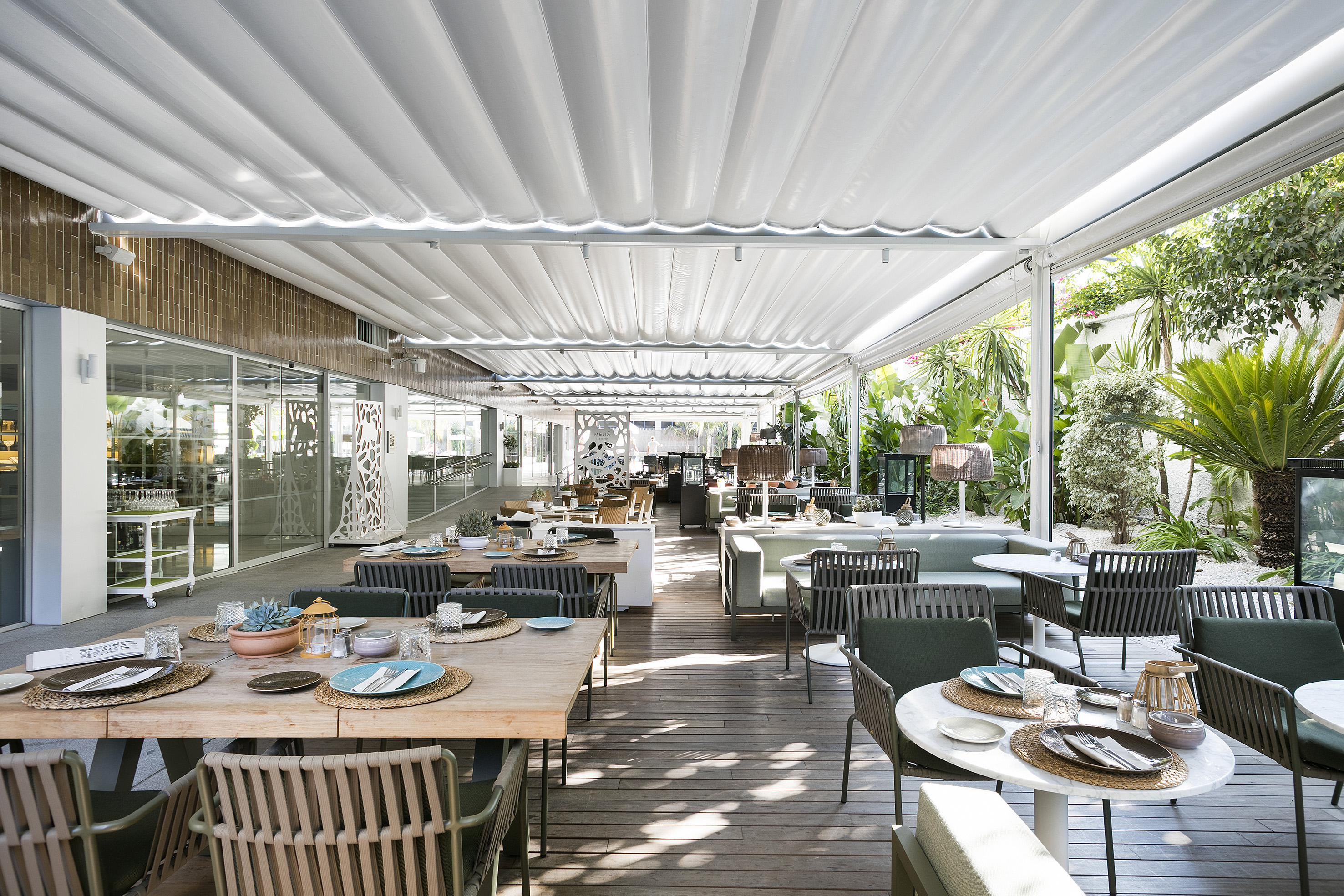 Modern outdoor restaurant terrace with retractable awning and garden.
