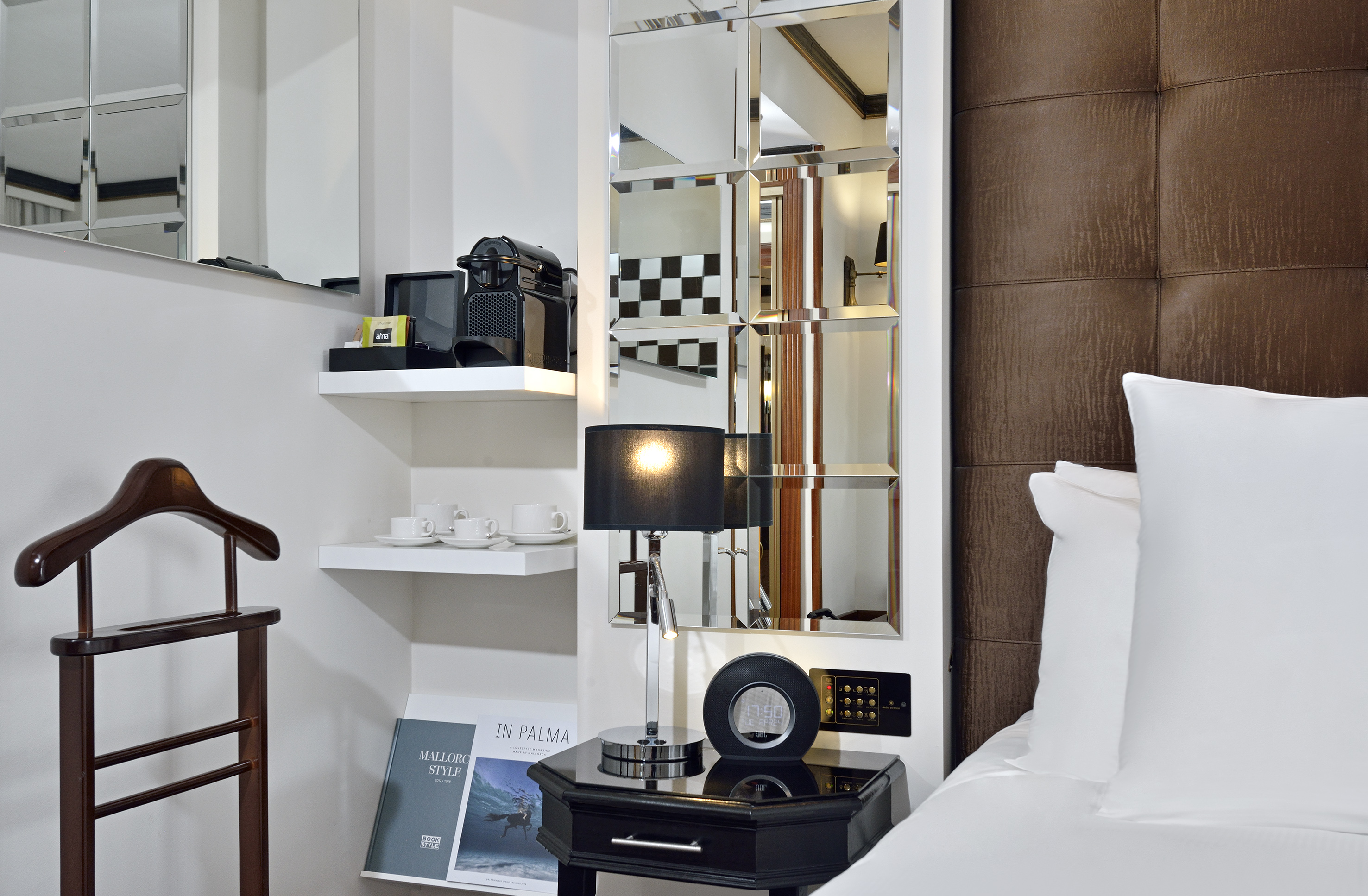 Modern hotel room with Nespresso, black lamp, mirror, and brown padded headboard.