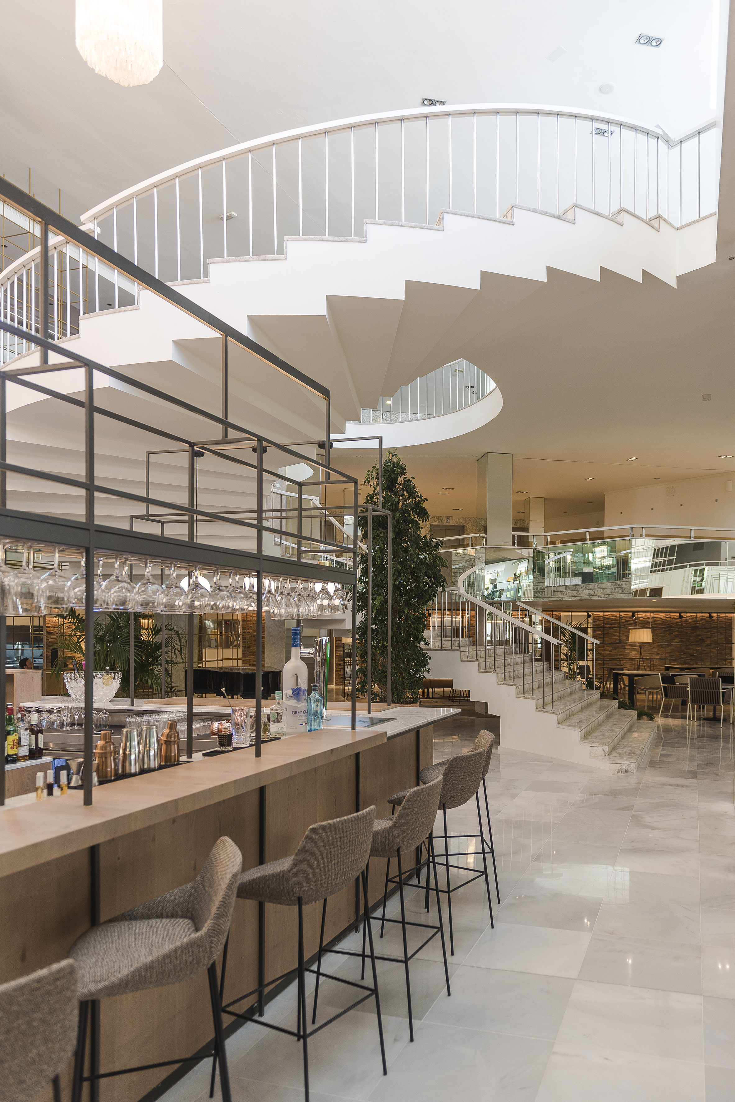 Modern hotel lobby bar with elegant spiral staircase and marble flooring.