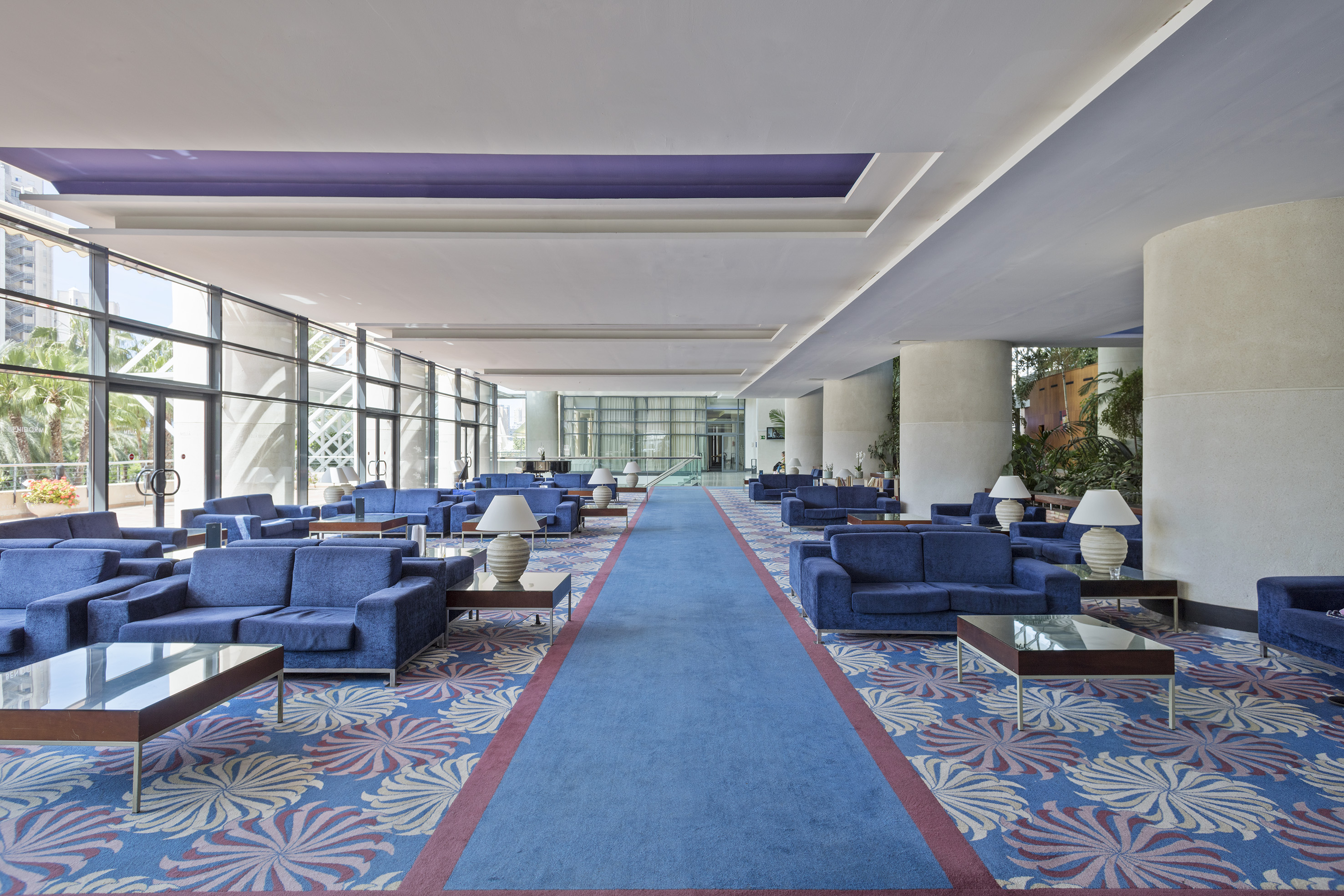 Hotel lobby with blue sofas, vibrant patterned carpet, and large windows.