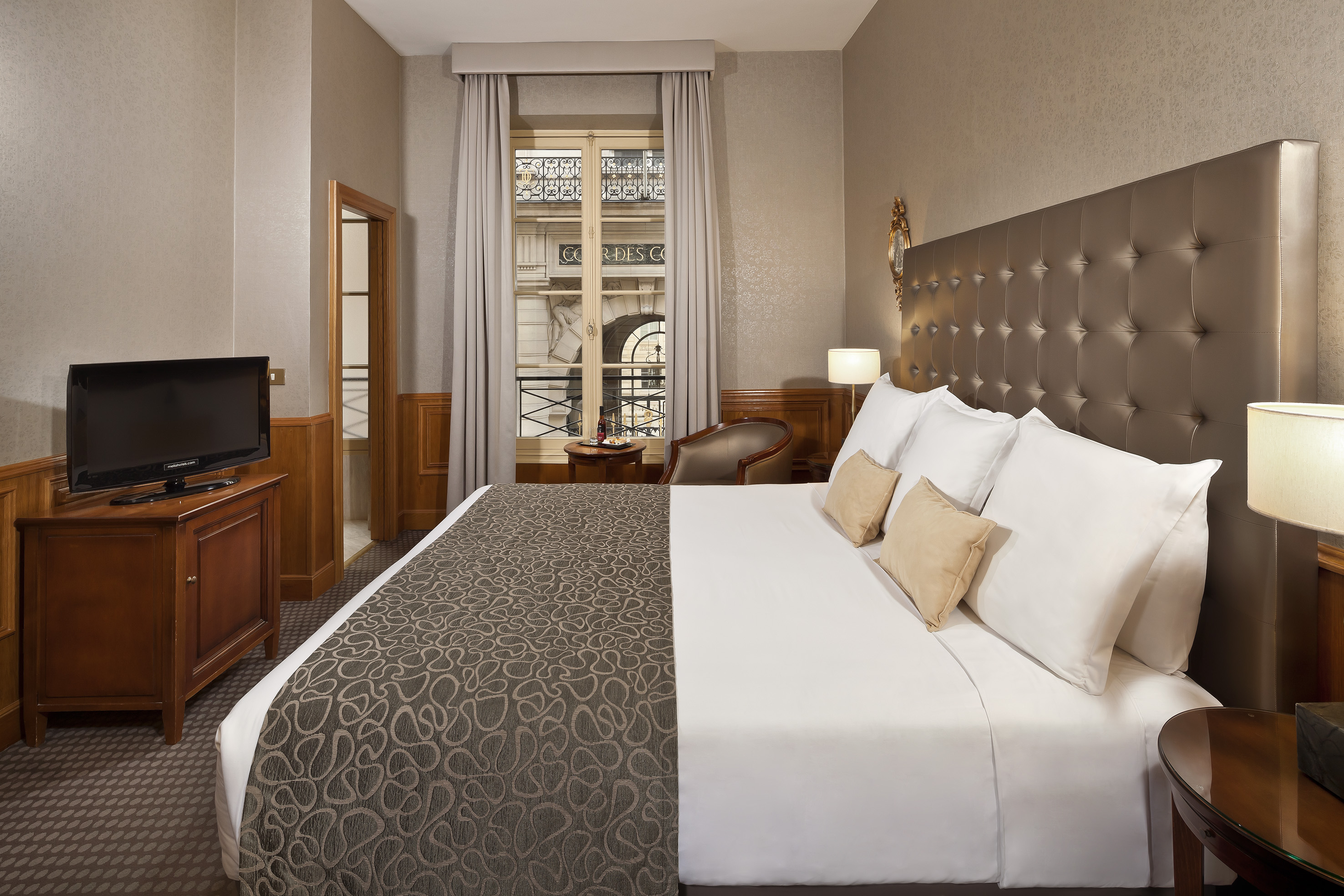 Hotel room with king bed, brown tufted headboard, and window city view.