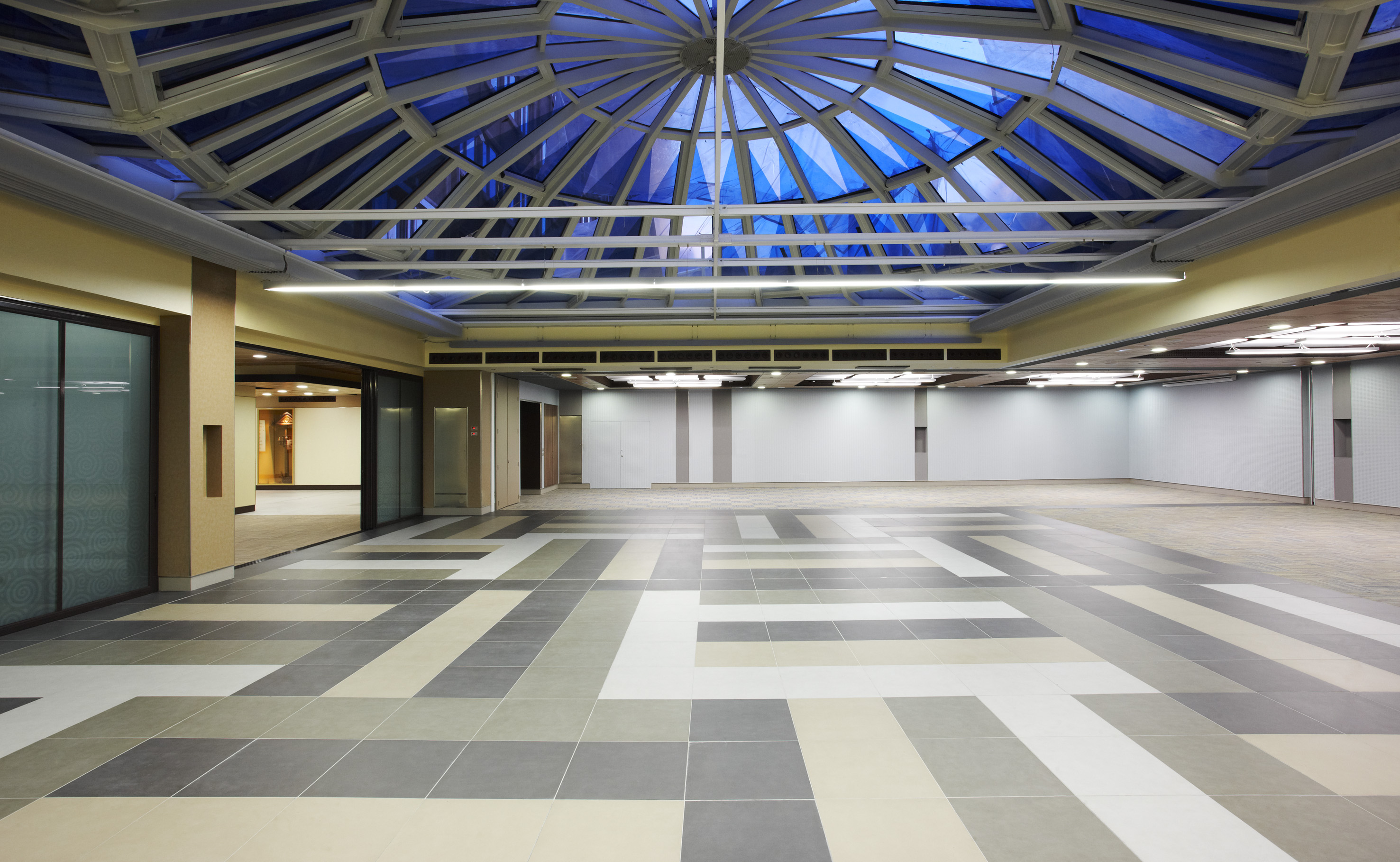 Modern empty atrium with blue glass dome skylight and geometric tiled floor.