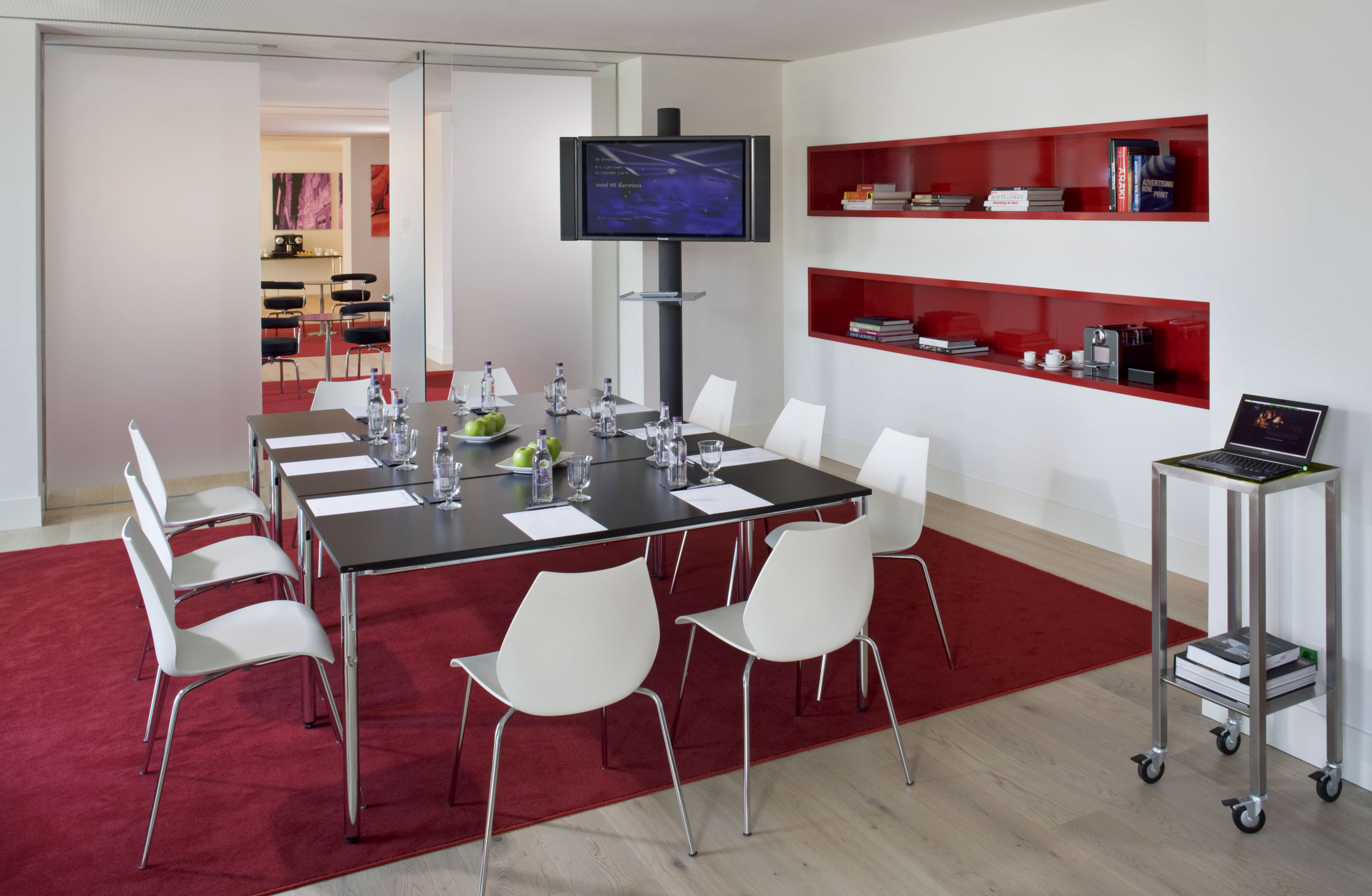 Modern conference room with black table, white chairs, TV, and red shelving.
