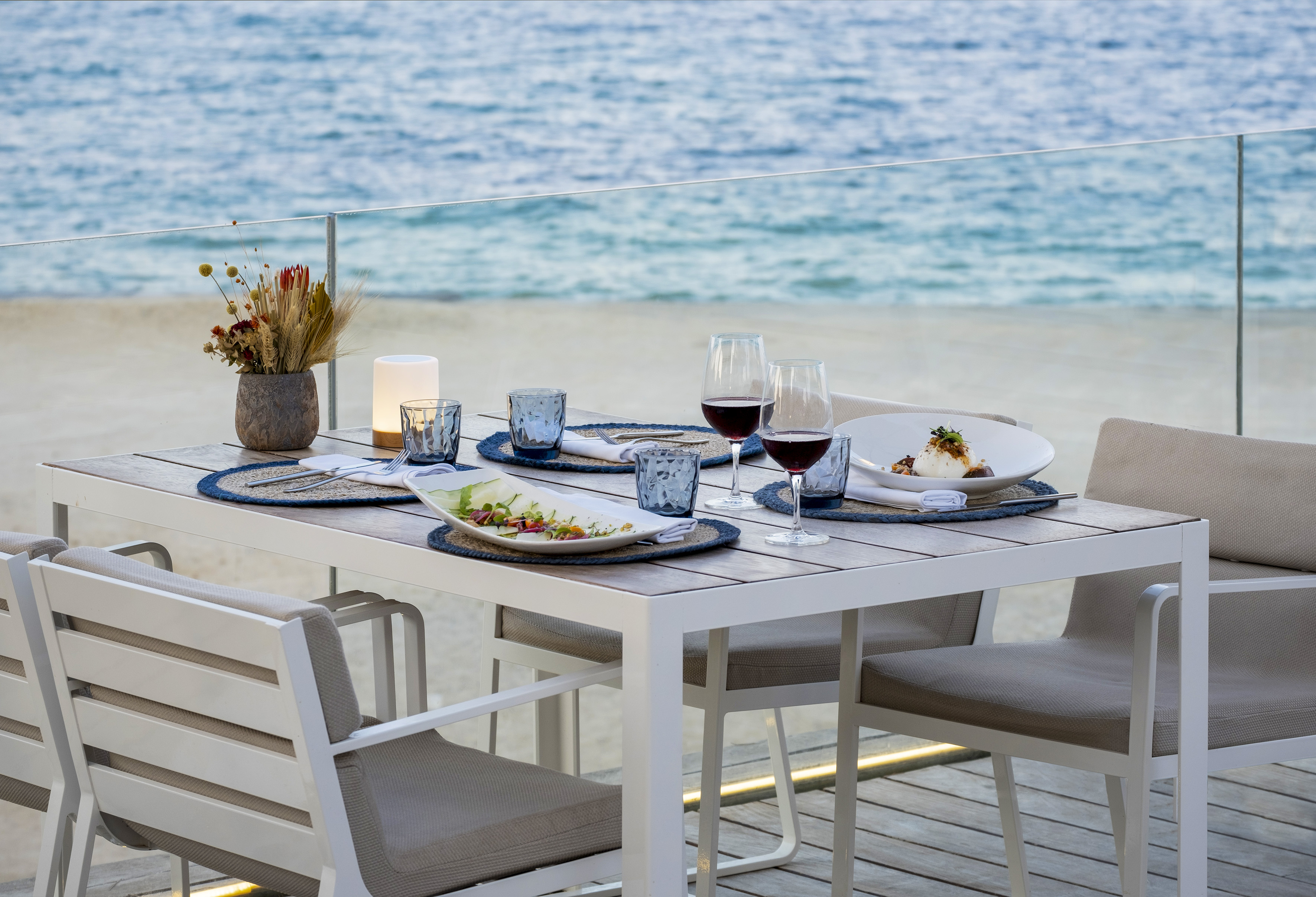 Beachfront outdoor dining table with food, wine, and ocean view.