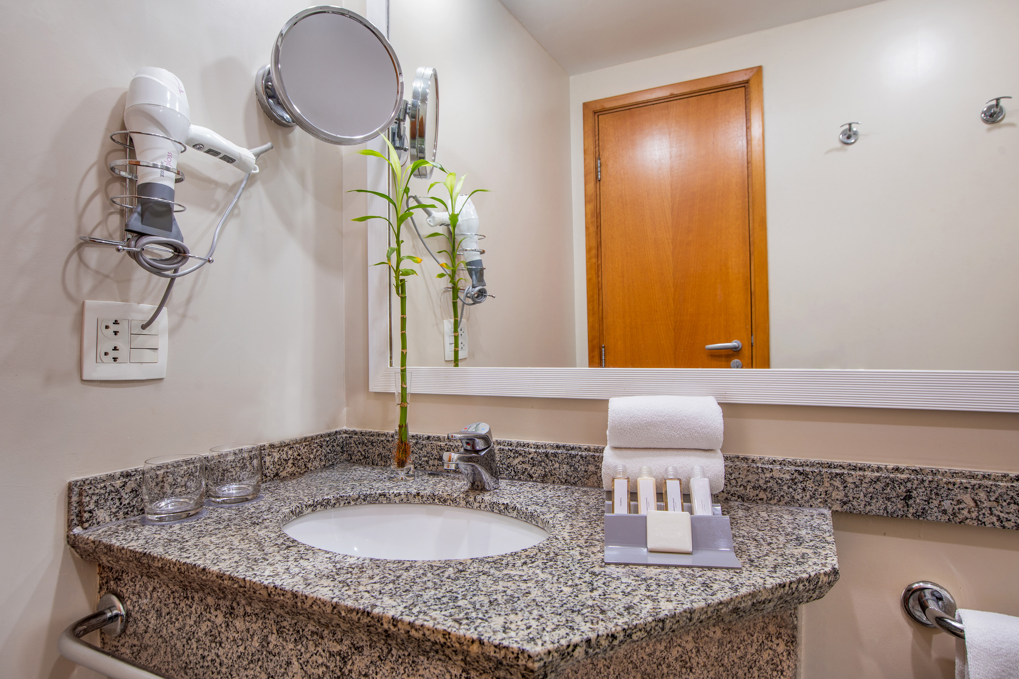 Bathroom vanity with granite counter, sink, mirror, hairdryer, and hotel toiletries.
