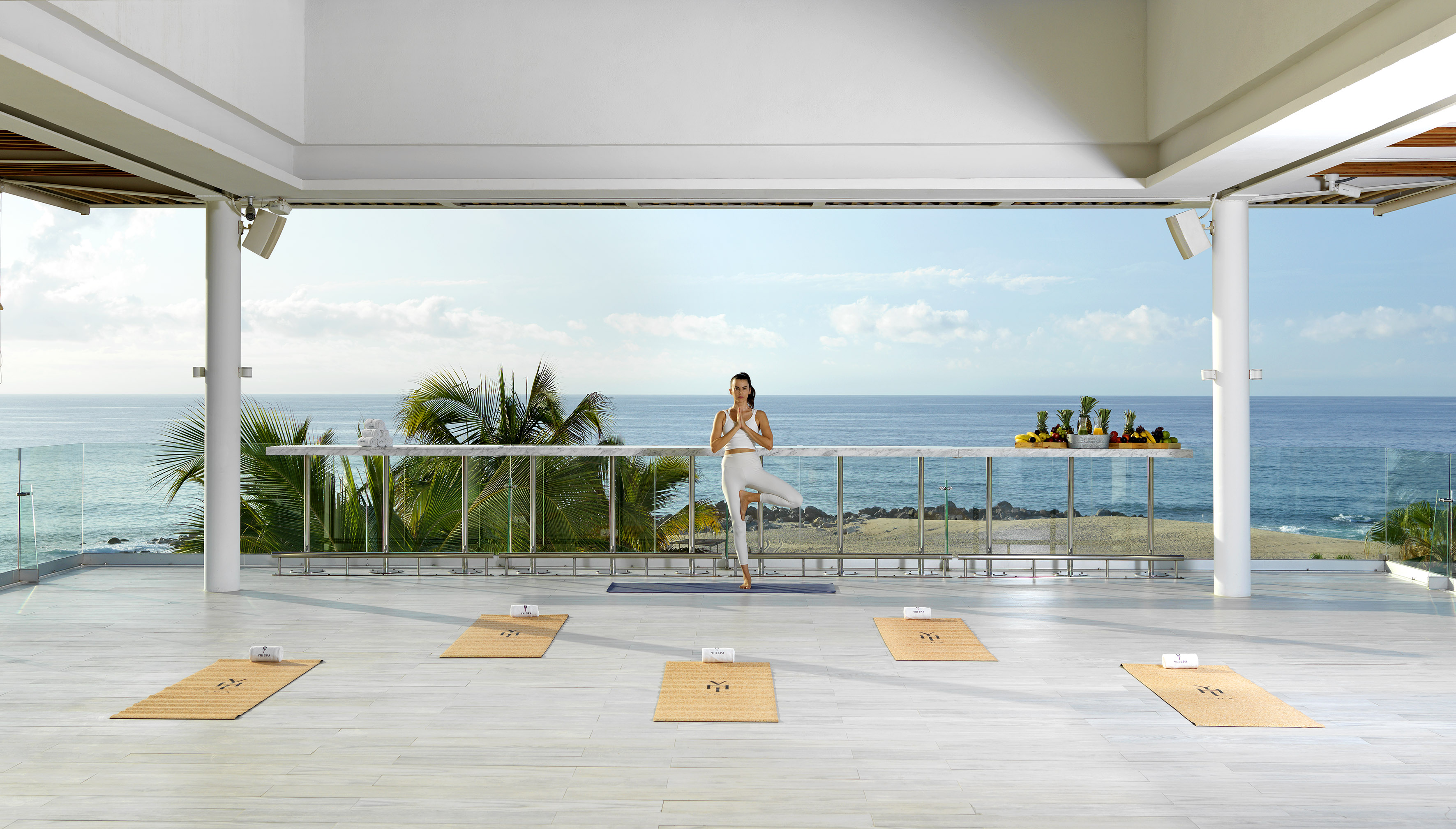 Open-air yoga studio overlooking ocean, woman in tree pose, tropical setting.