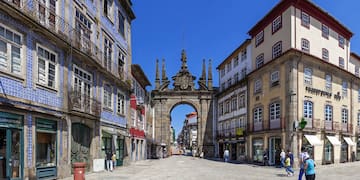 a stone archway in a street with buildings and people walking with Arco da Porta Nova in the background