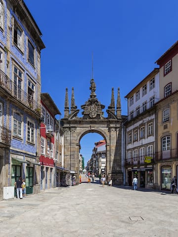a stone archway in a street with buildings and people walking with Arco da Porta Nova in the background