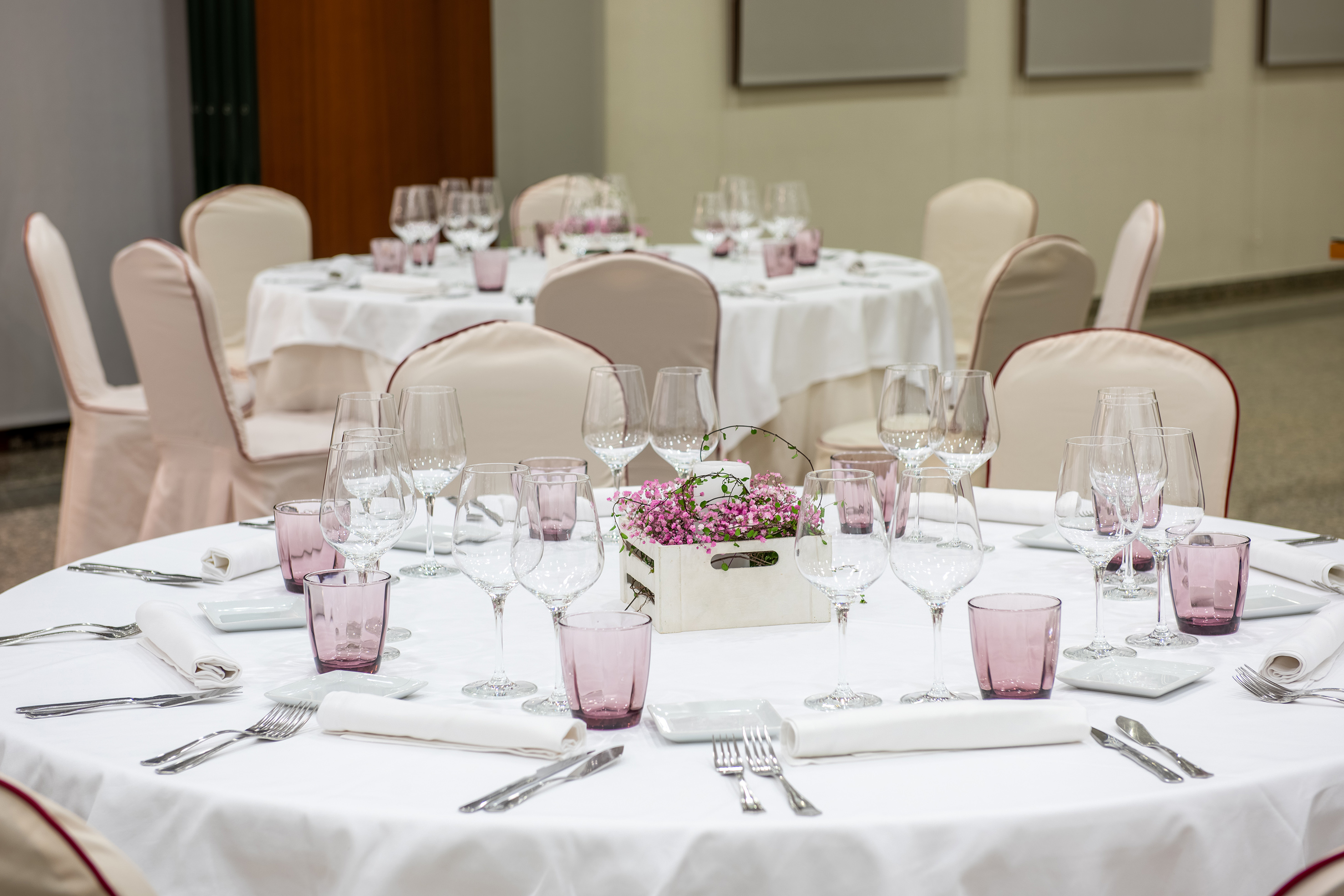 Elegant event tables with white linens, wine glasses, and pink floral centerpieces.