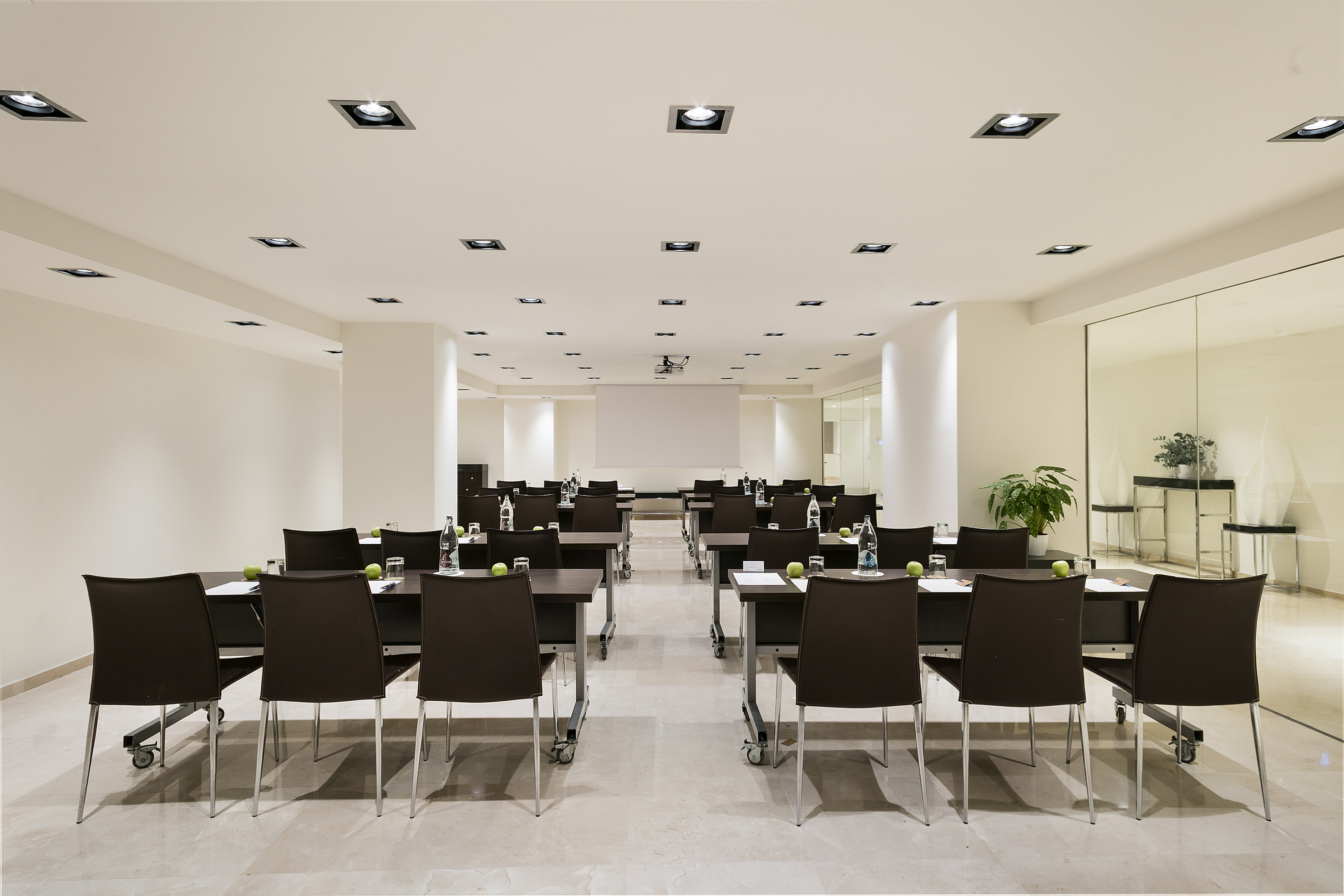 Modern conference room with tables, chairs, projector, and refreshments.