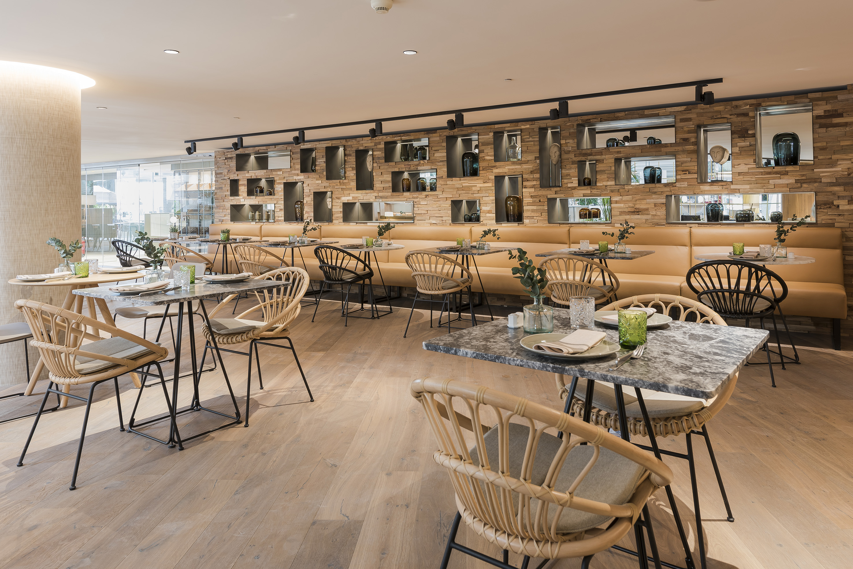Modern restaurant dining room with rattan chairs, marble tables, and a wood wall.