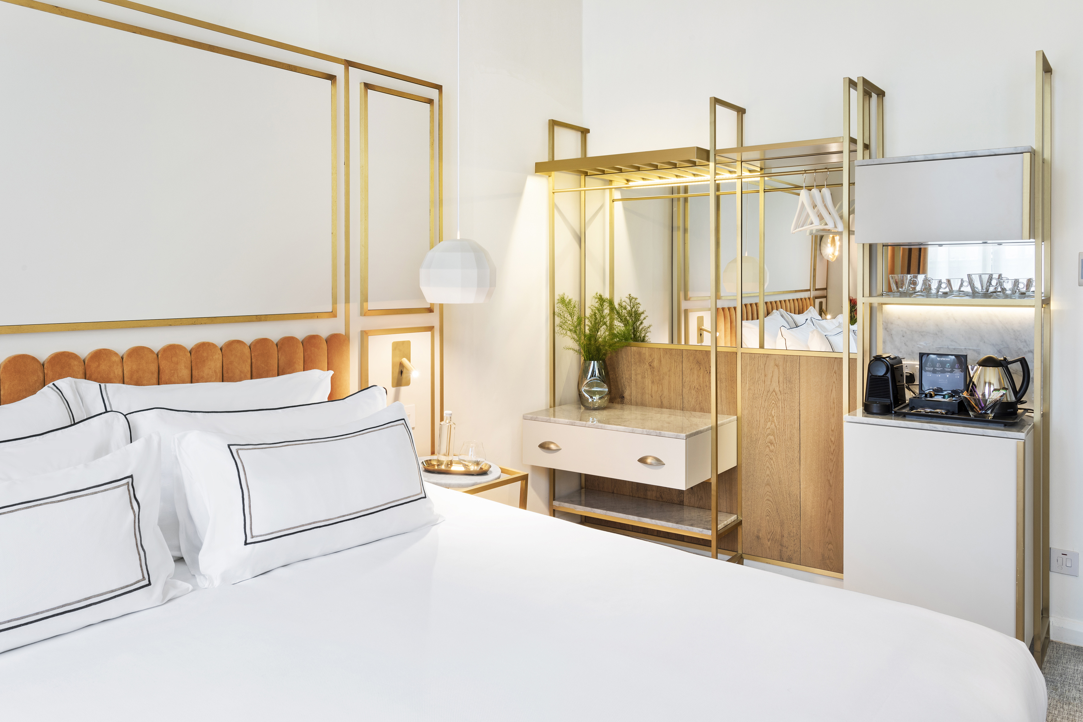 Modern hotel room, white bed, orange headboard, gold accents, coffee bar.