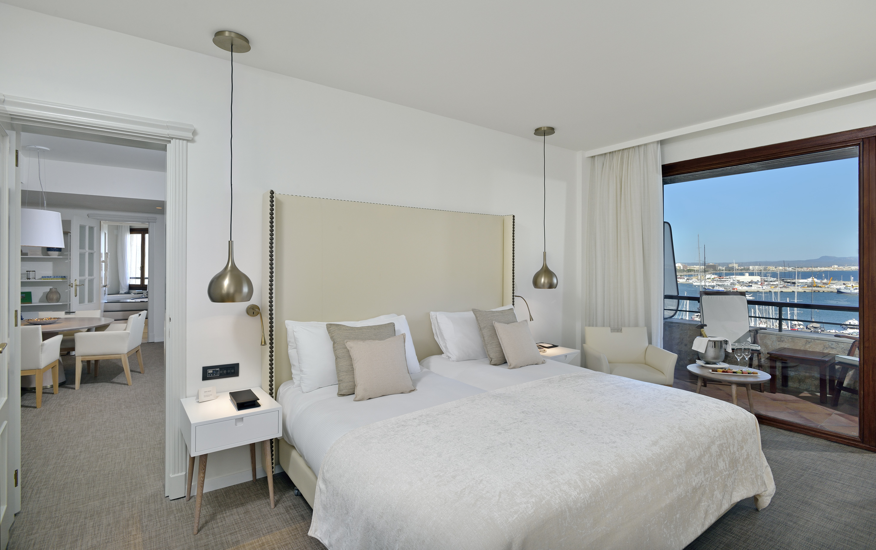 Modern hotel bedroom with marina view balcony and cozy sitting area.