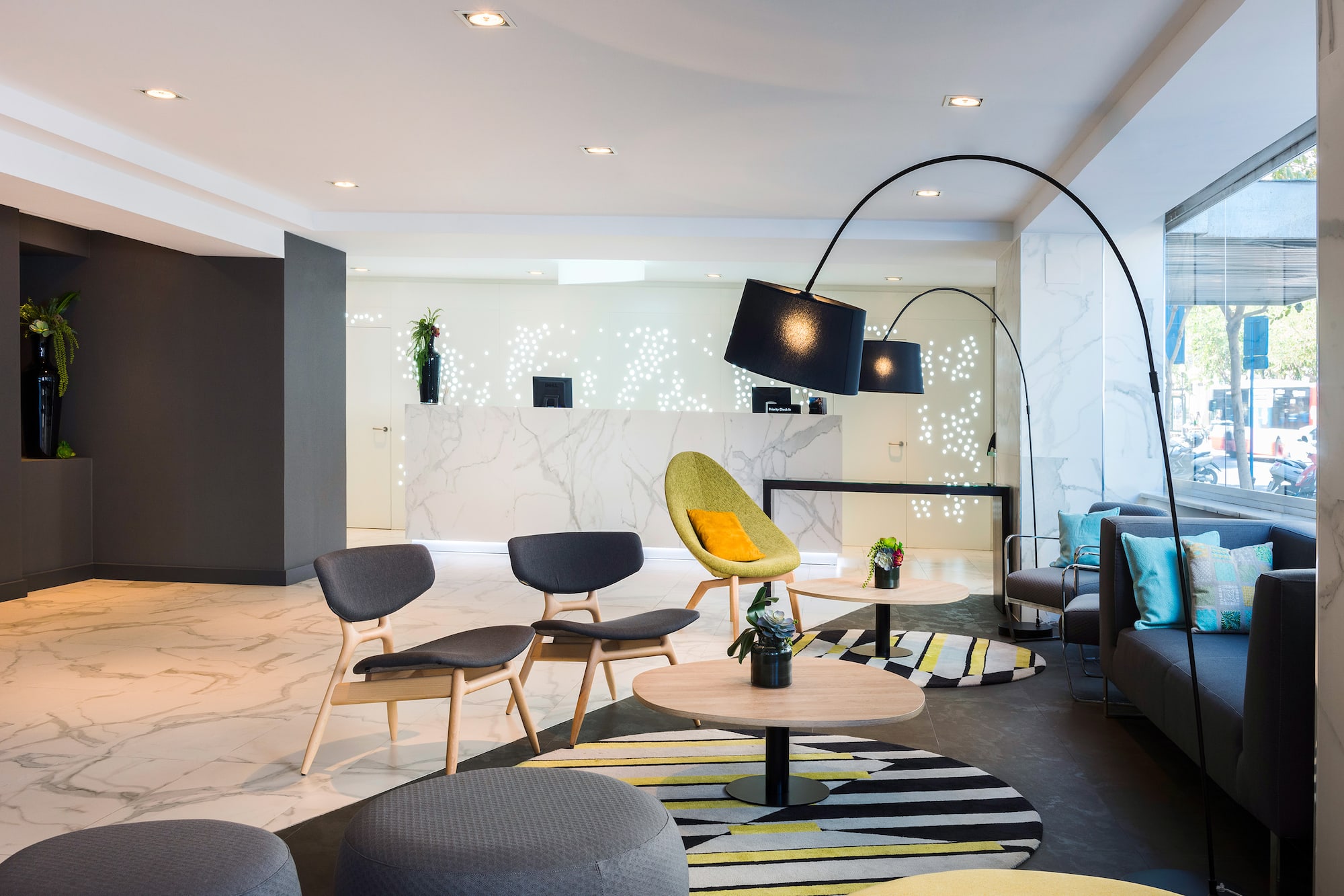 Modern hotel lobby with marble reception, lounge chairs, and patterned rugs.