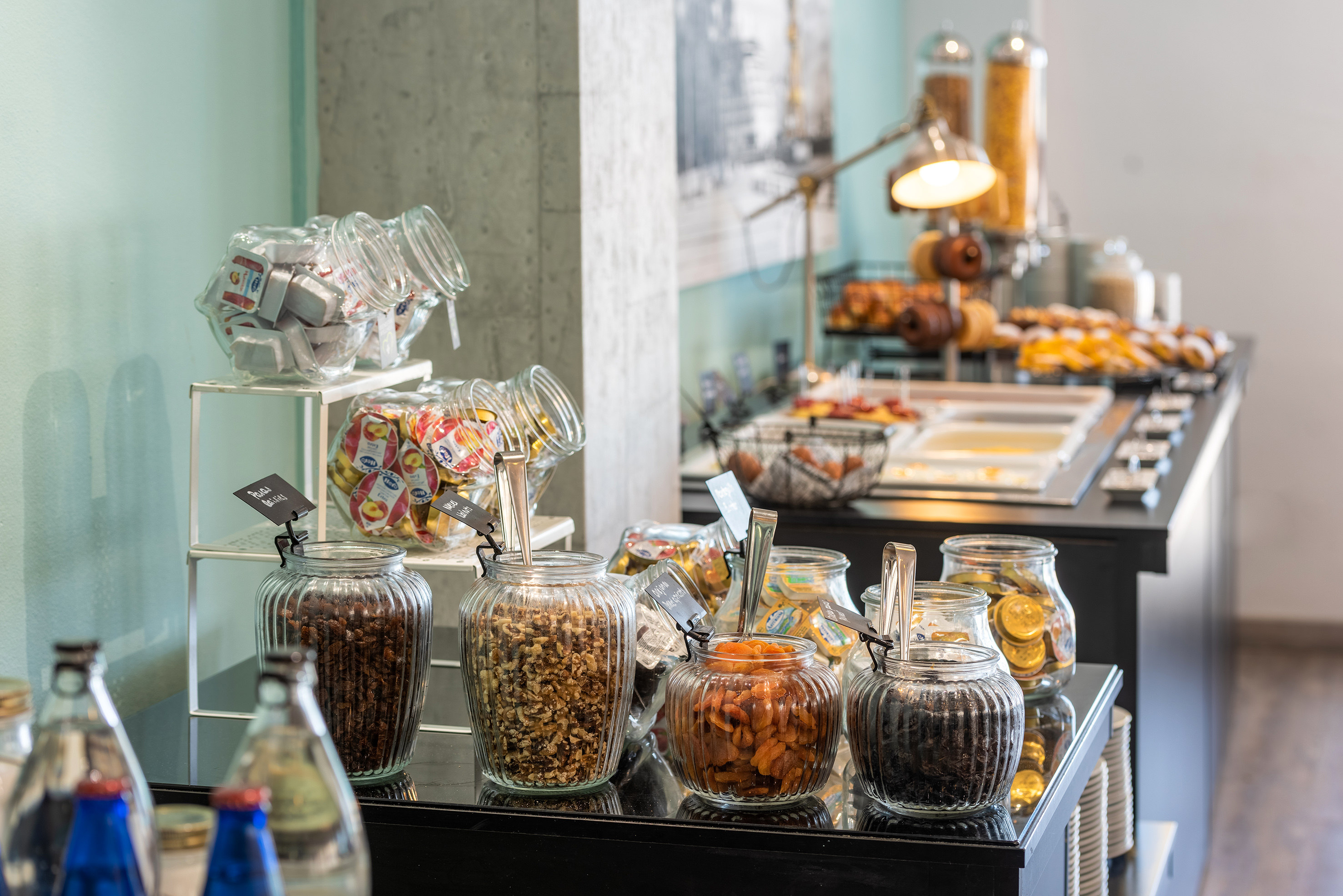 Breakfast buffet with jars of dried fruit, nuts, jams, pastries, and cereals.