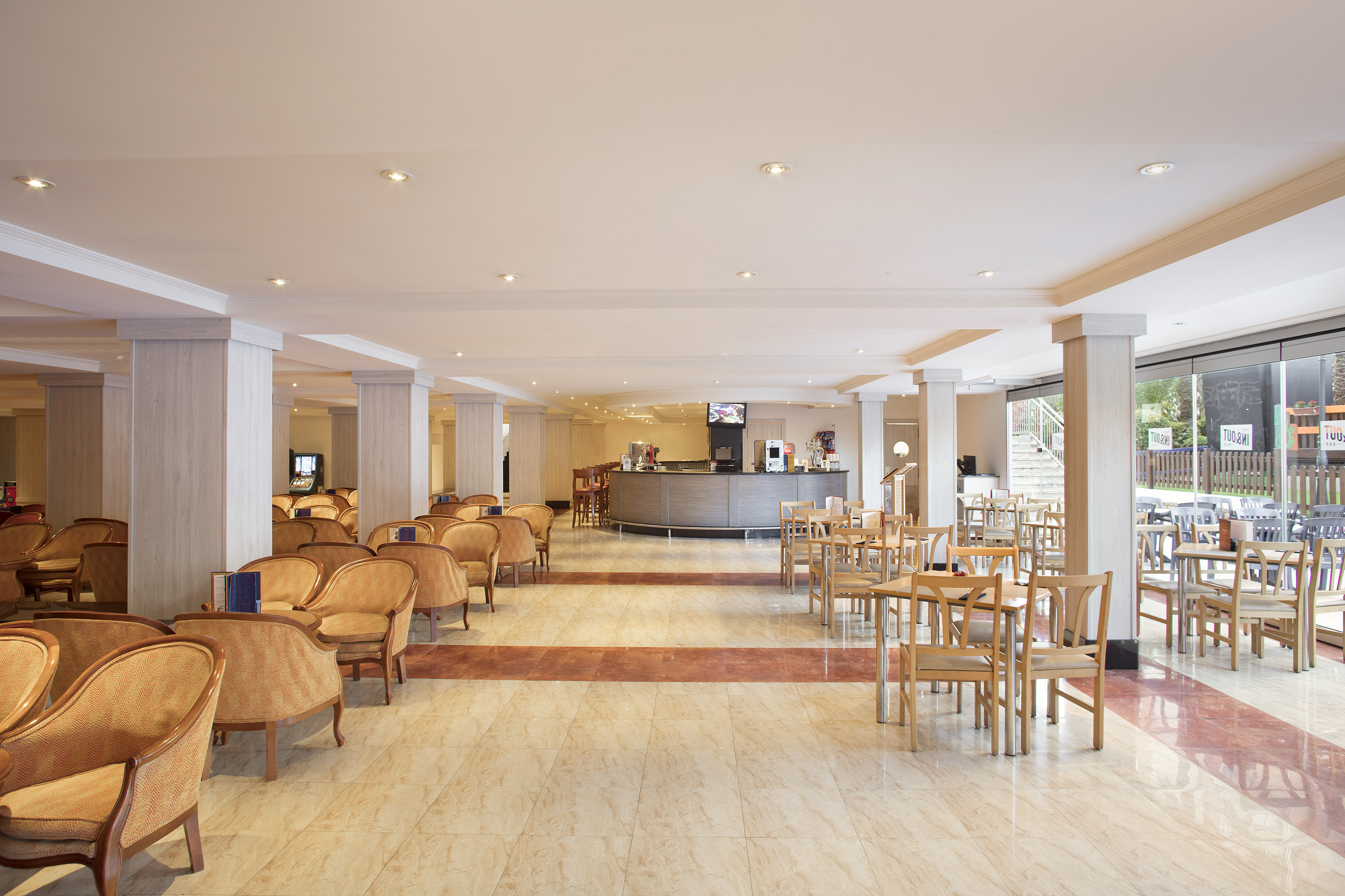 Hotel lounge with bar, armchairs, and dining tables on a bright tiled floor.