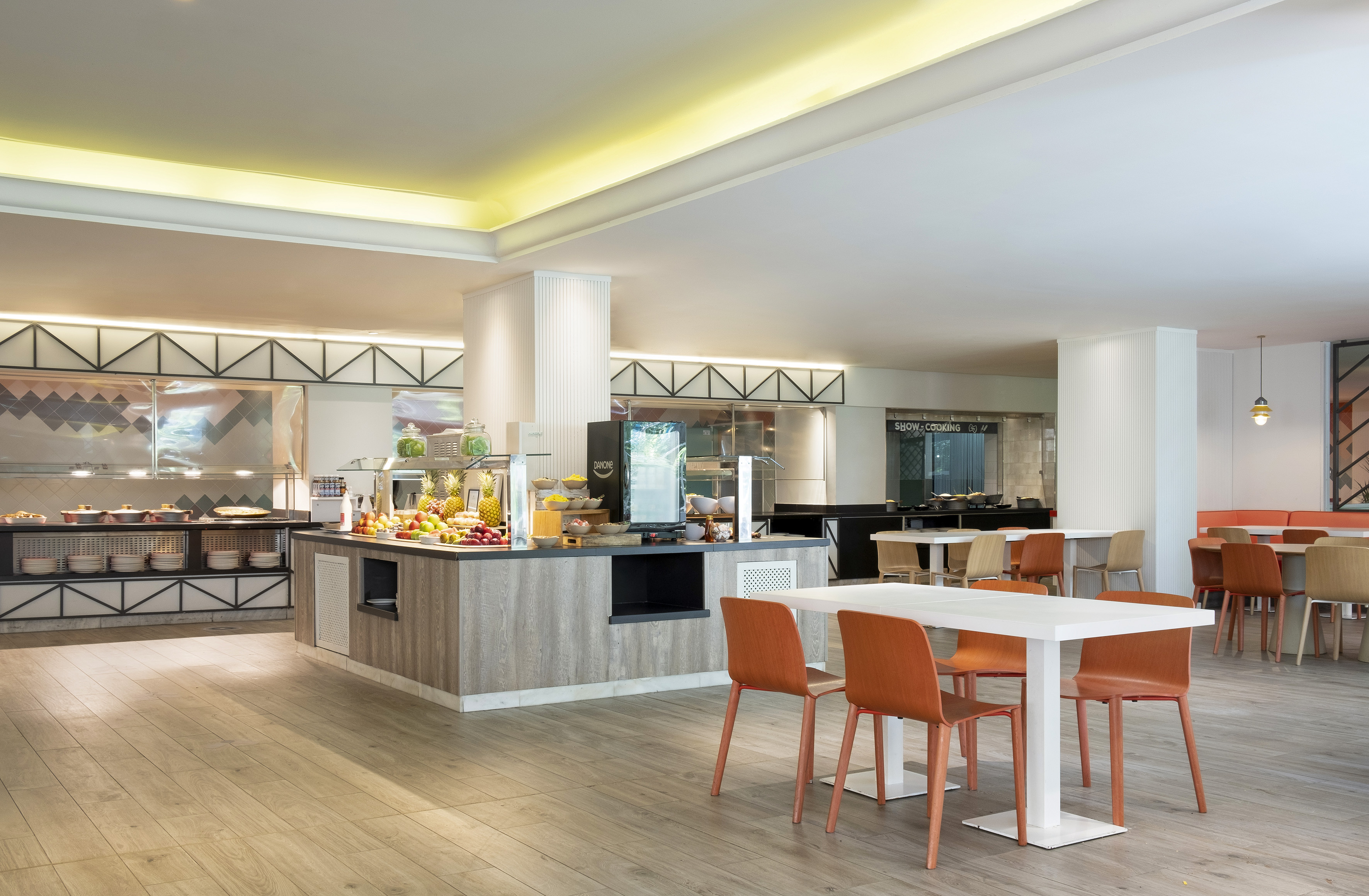 Modern hotel buffet restaurant with fresh fruit, hot dishes, and dining tables.