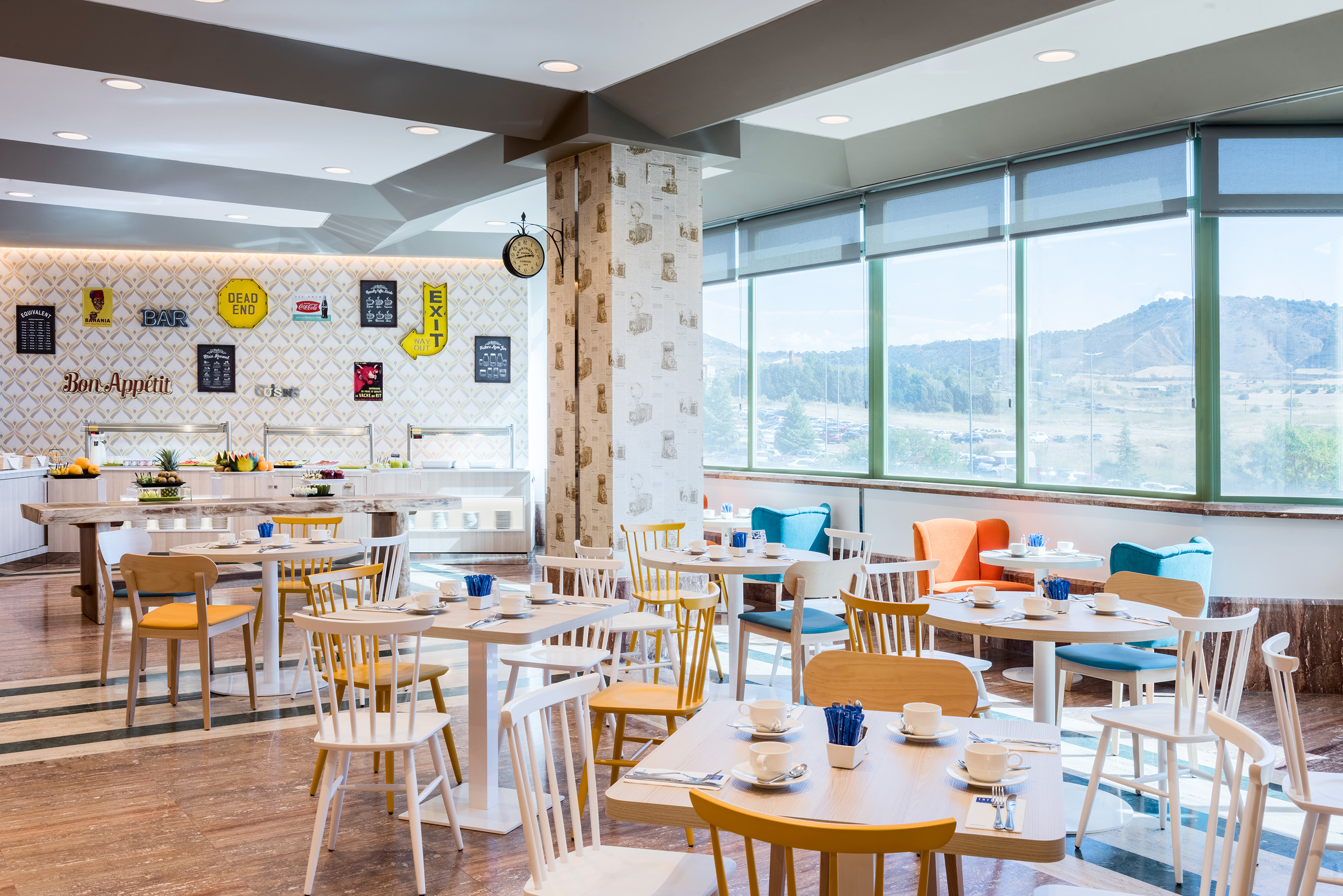 Bright restaurant buffet with colorful chairs, large windows, and a mountain view.