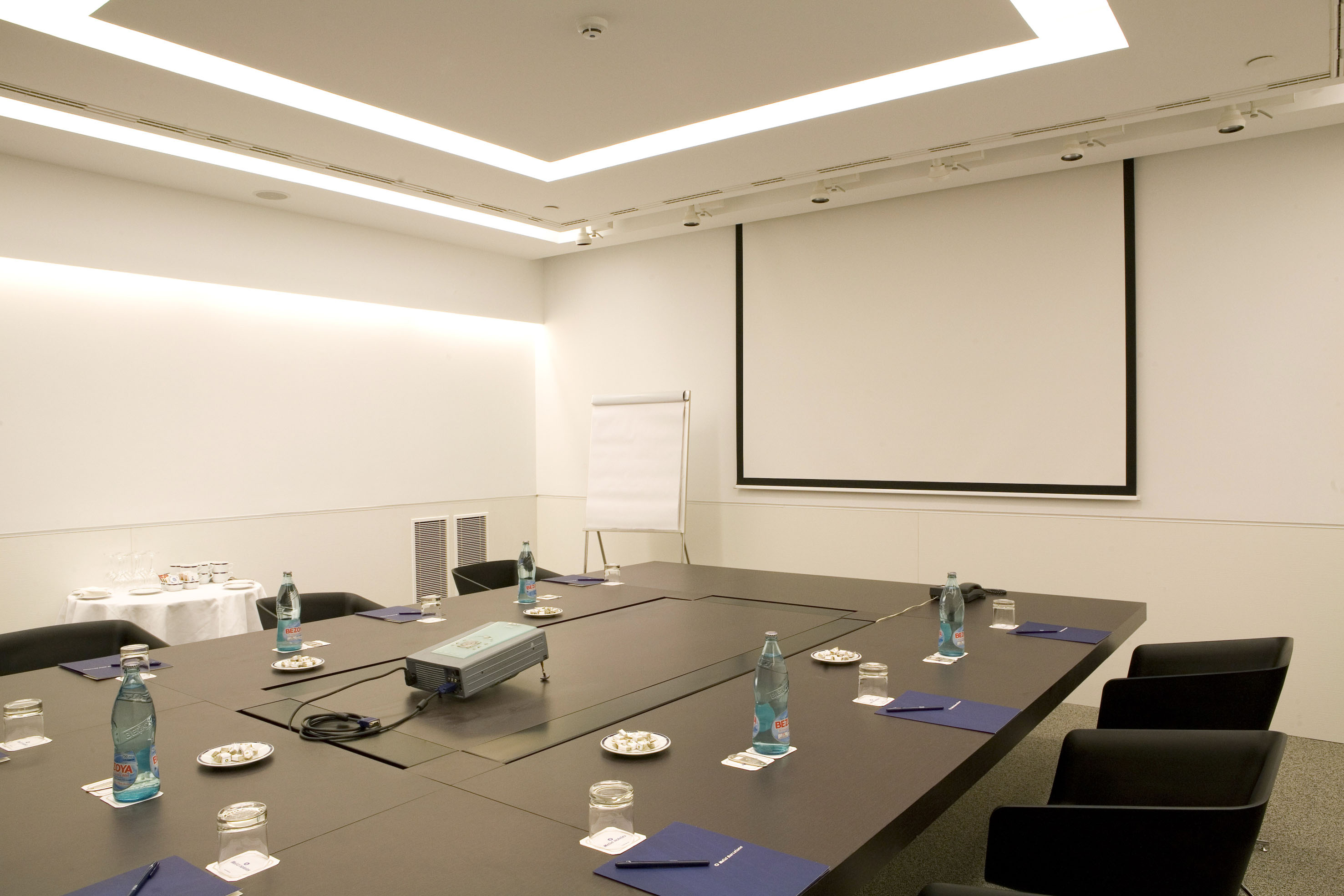 Professional meeting room with projector, screen, large table, and chairs.