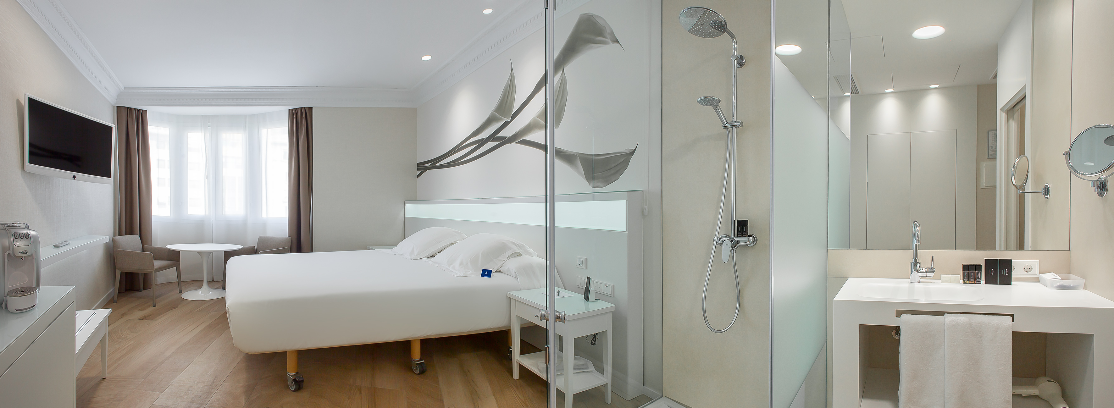 Modern hotel room with bed, TV, wood floor, and integrated glass shower.
