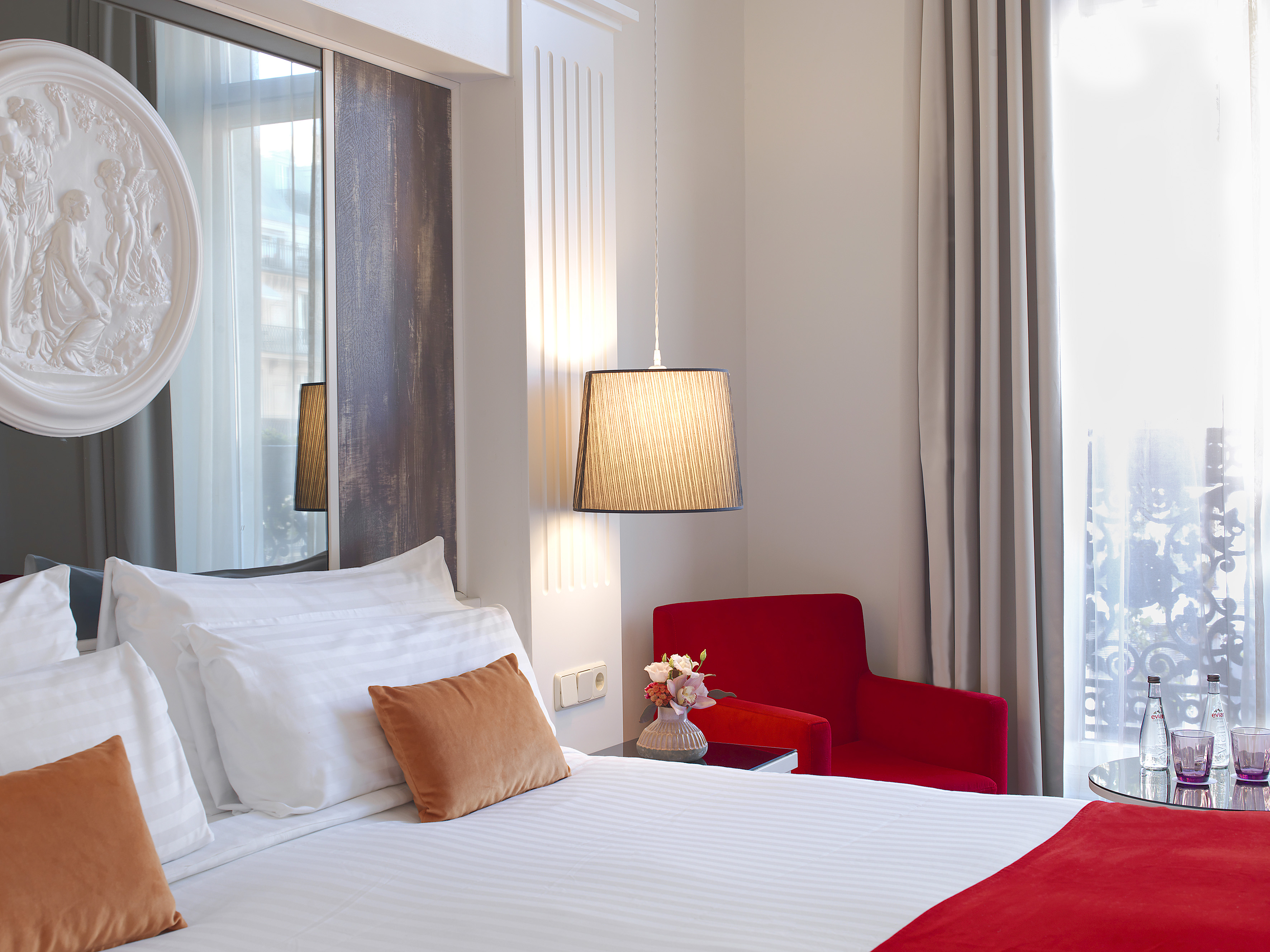 Luxurious bedroom interior featuring white bed, red chair, and unique wall art.