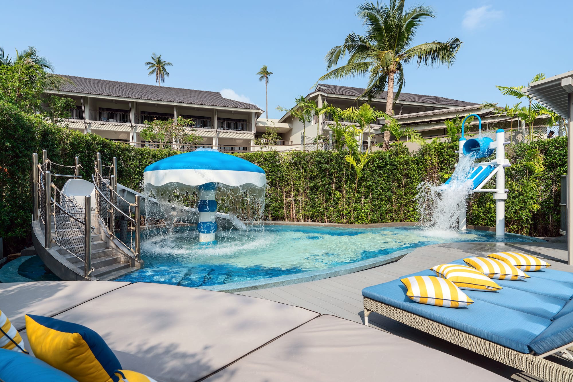 Hotel kids' pool with umbrella fountain, water slide, and daybeds.