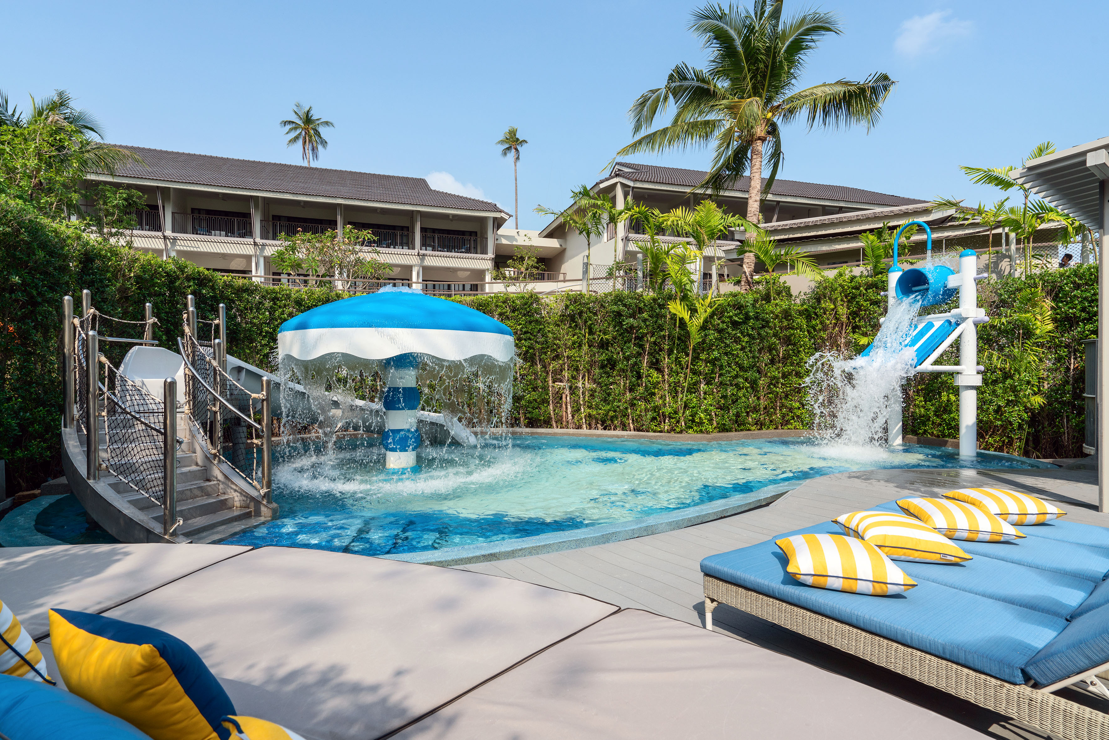 Hotel kids' pool with umbrella fountain, water slide, and daybeds.