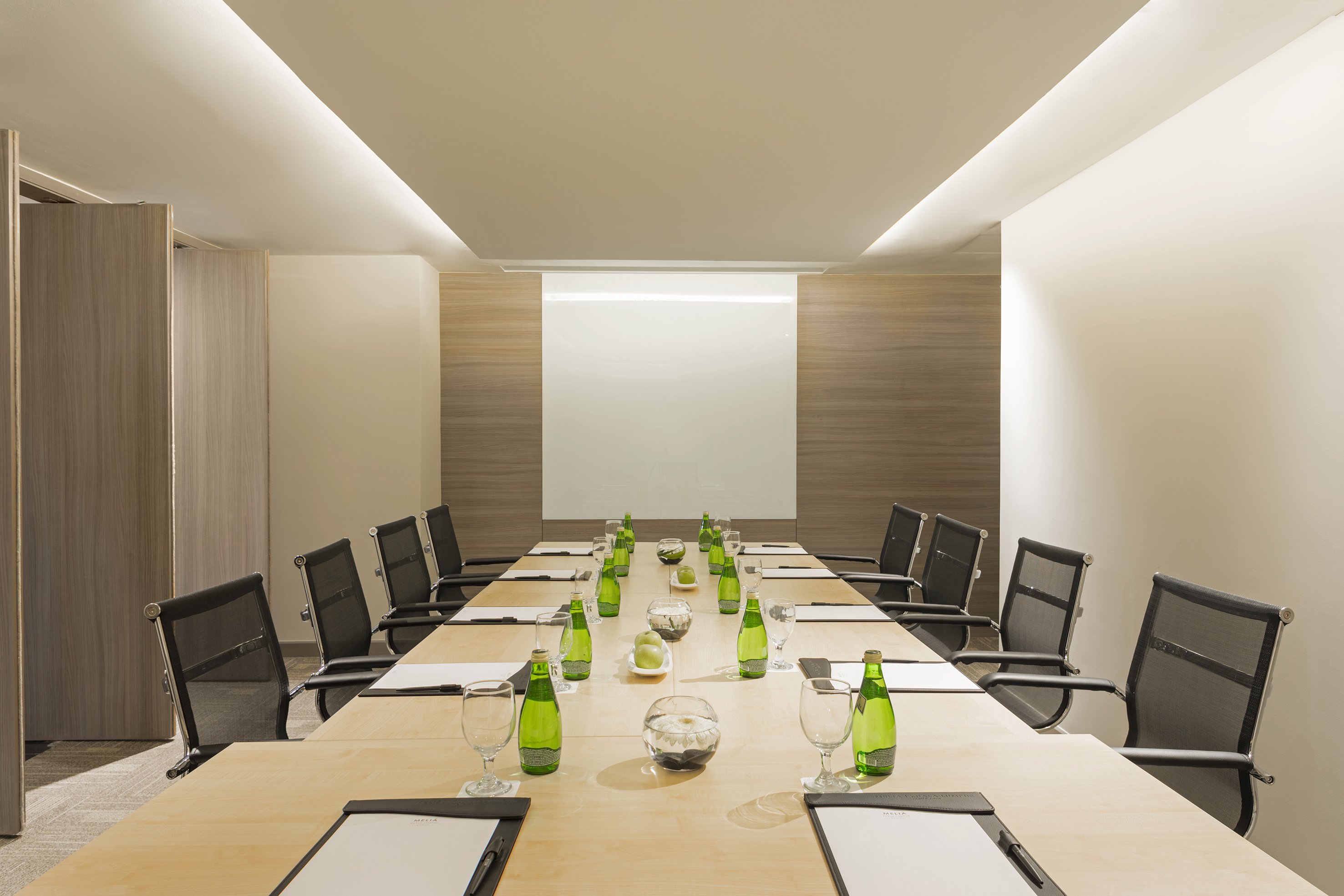 Modern corporate meeting room with light wood table, black chairs, and whiteboard.