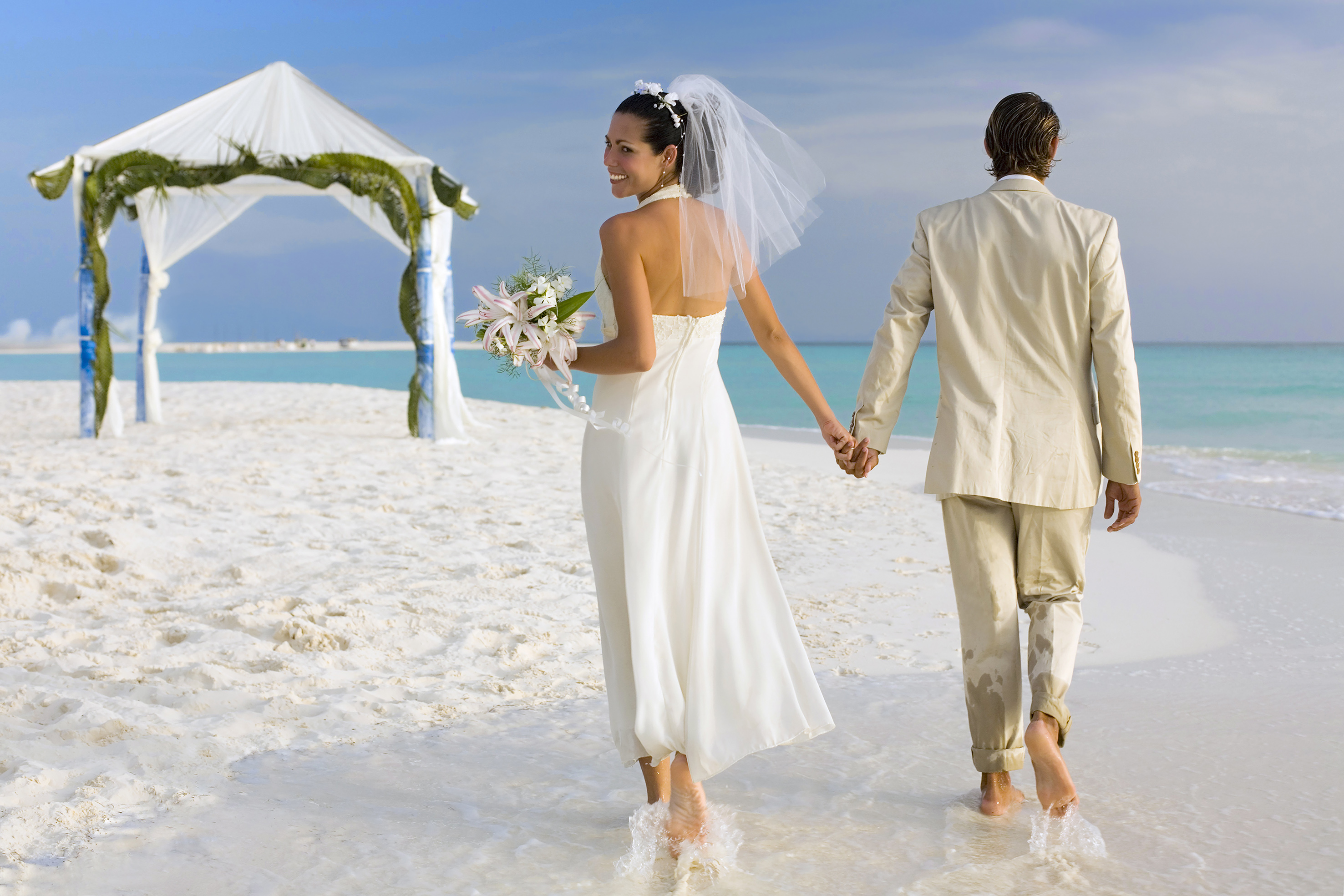 a man and woman holding hands and walking on a beach