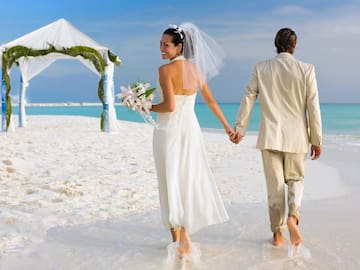 a man and woman holding hands and walking on a beach