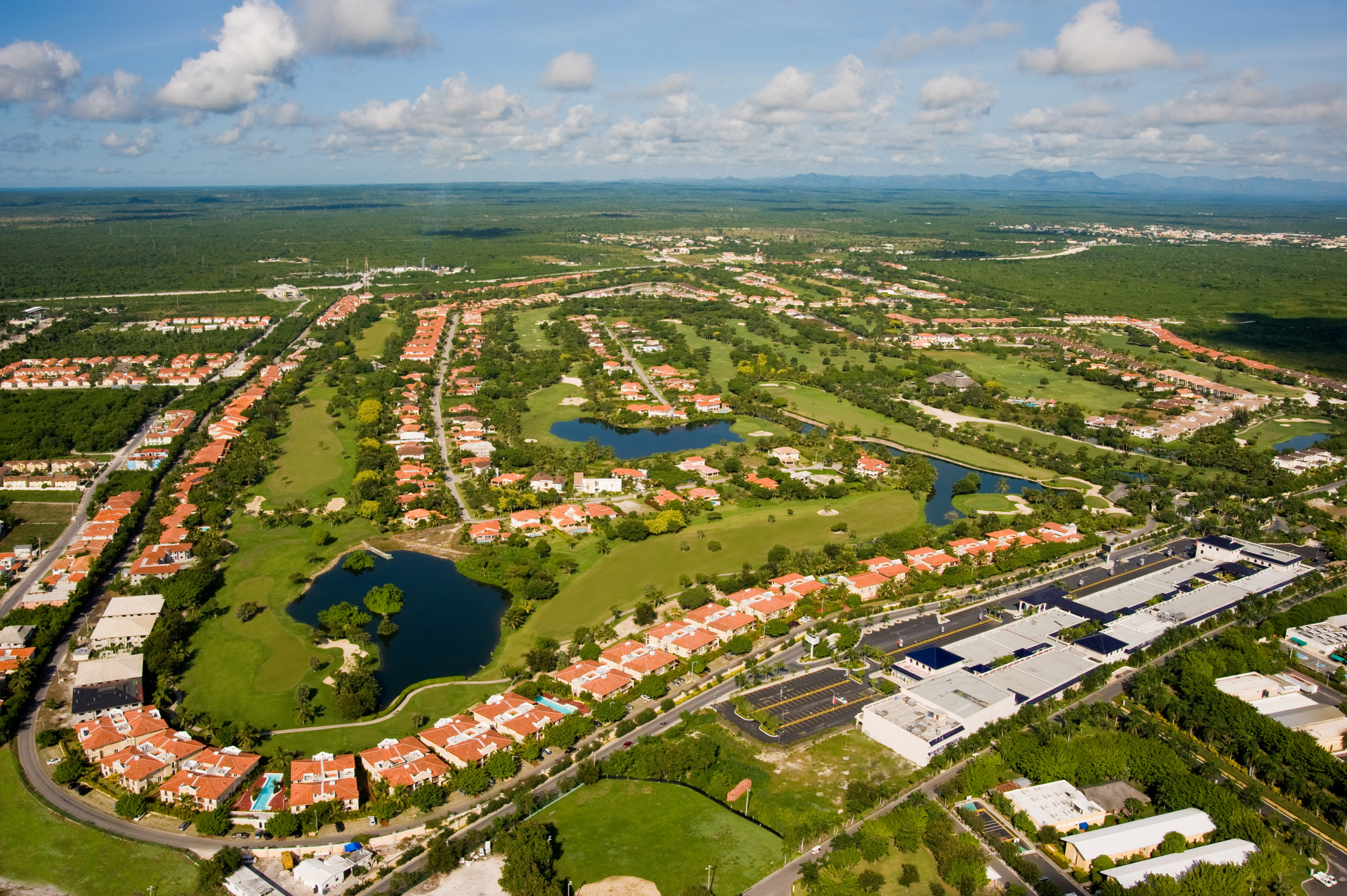 Aerial of golf community: red-roofed homes, lakes, and commercial complex.