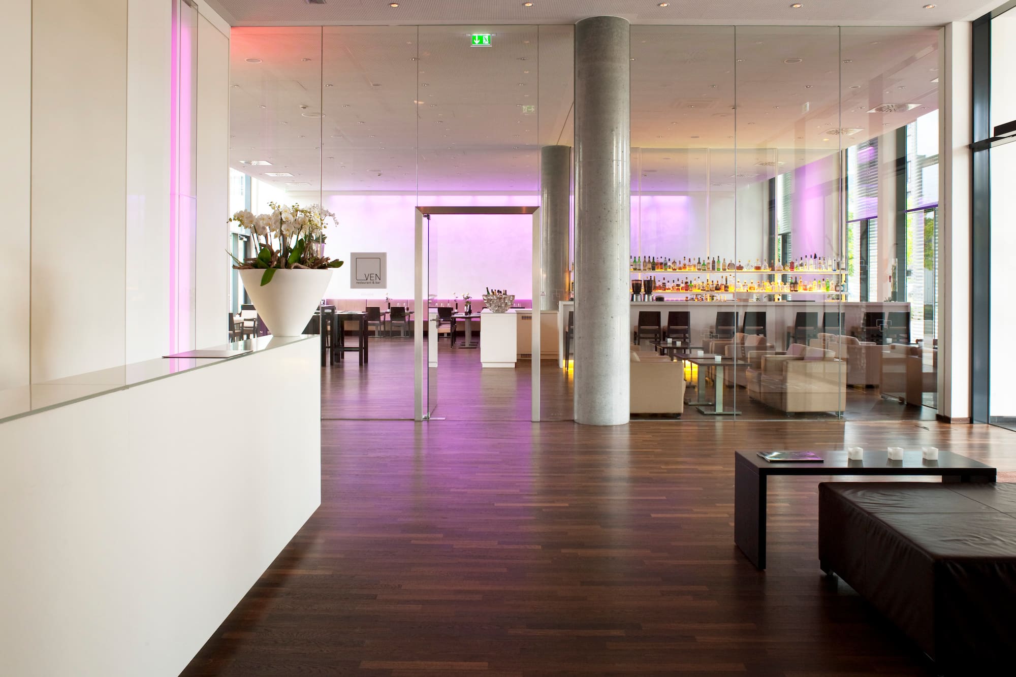 Modern hotel lobby and bar with white reception, glass walls, and lounge seating.